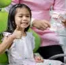 At Happy Smiles Orthodontics in St. Augustine, FL, a young girl sits in a chair and gives a thumbs up as an adult hands her a dental hygiene kit.