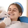 At Happy Smiles Orthodontics in St. Augustine, FL, a dentist wearing gloves adjusts braces for a smiling young patient in the dental chair.