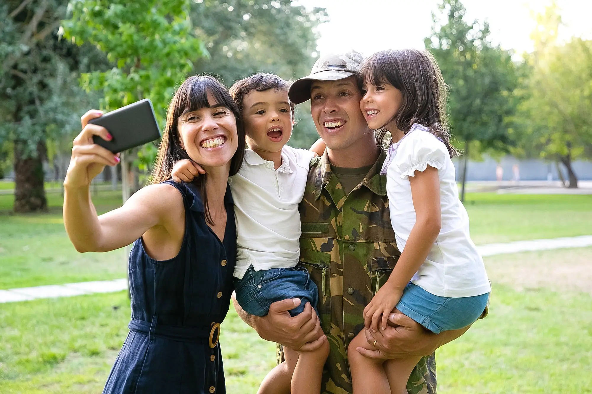 A family enjoys a selfie outdoors as a person in military uniform holds two children proudly showing their new metal braces—thanks to Happy Smiles Orthodontics in St. Augustine, FL—while an adult snaps the photo.