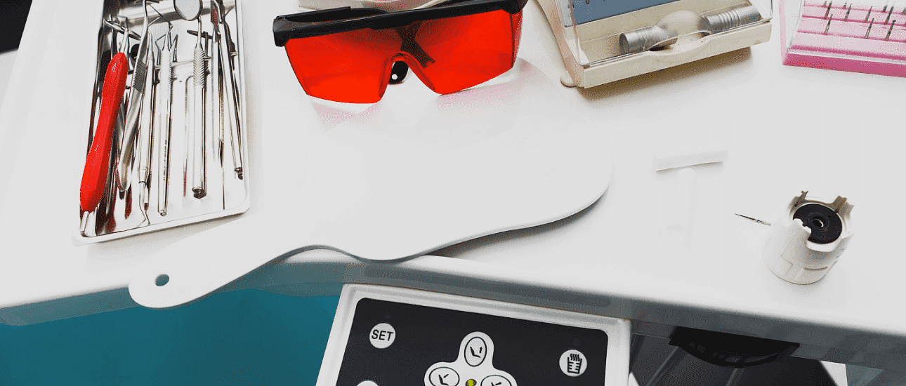 At Happy Smiles Orthodontics in St. Augustine, FL, a dentist's tray is neatly arranged on a white surface with dental tools, protective red glasses, a handheld mirror, metal braces, and a control panel.