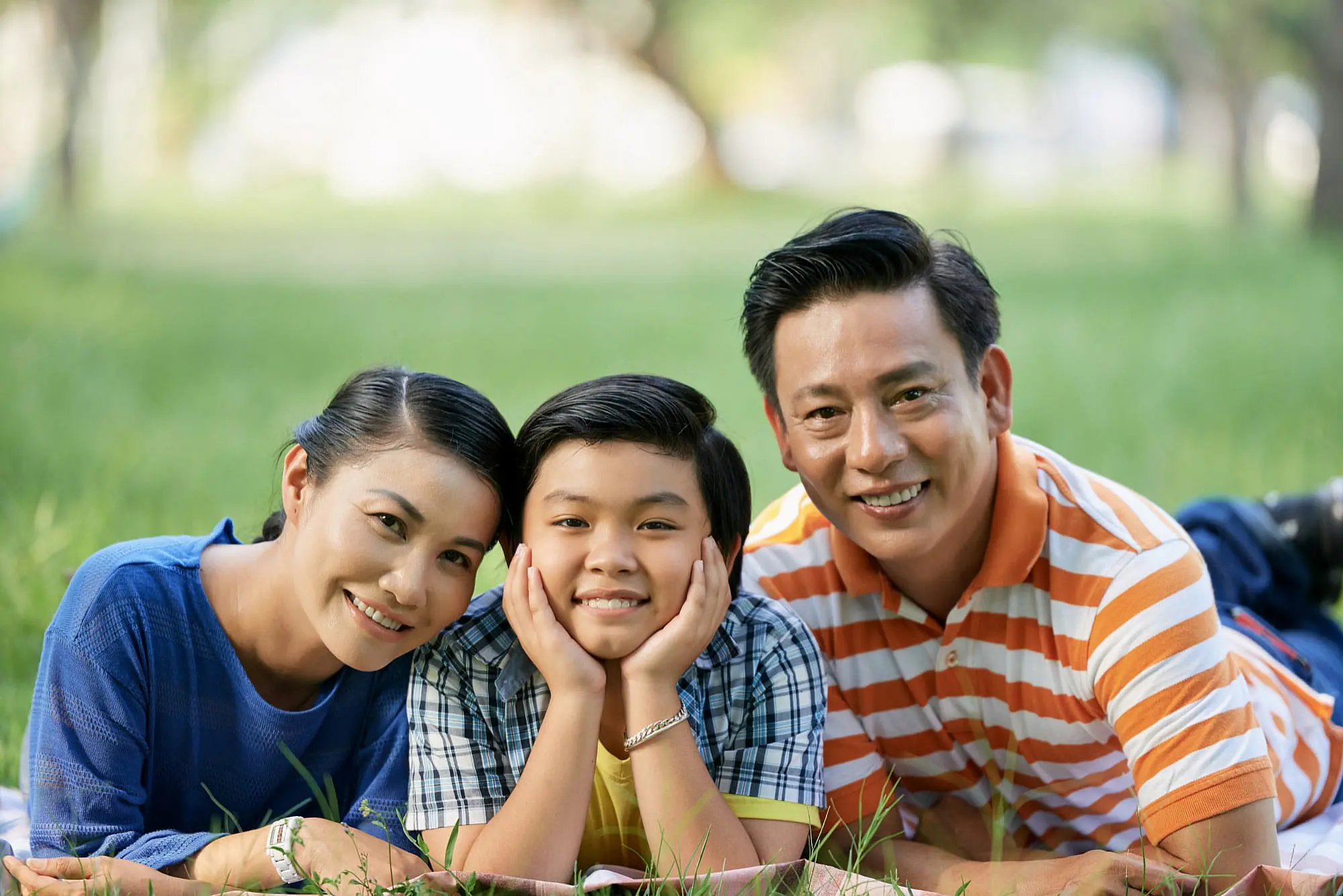 Relaxing on the grass outdoors in St. Augustine FL, two adults and a child smile confidently at the camera—showcasing the results of Invisalign insurance through Happy Smiles Orthodontics.