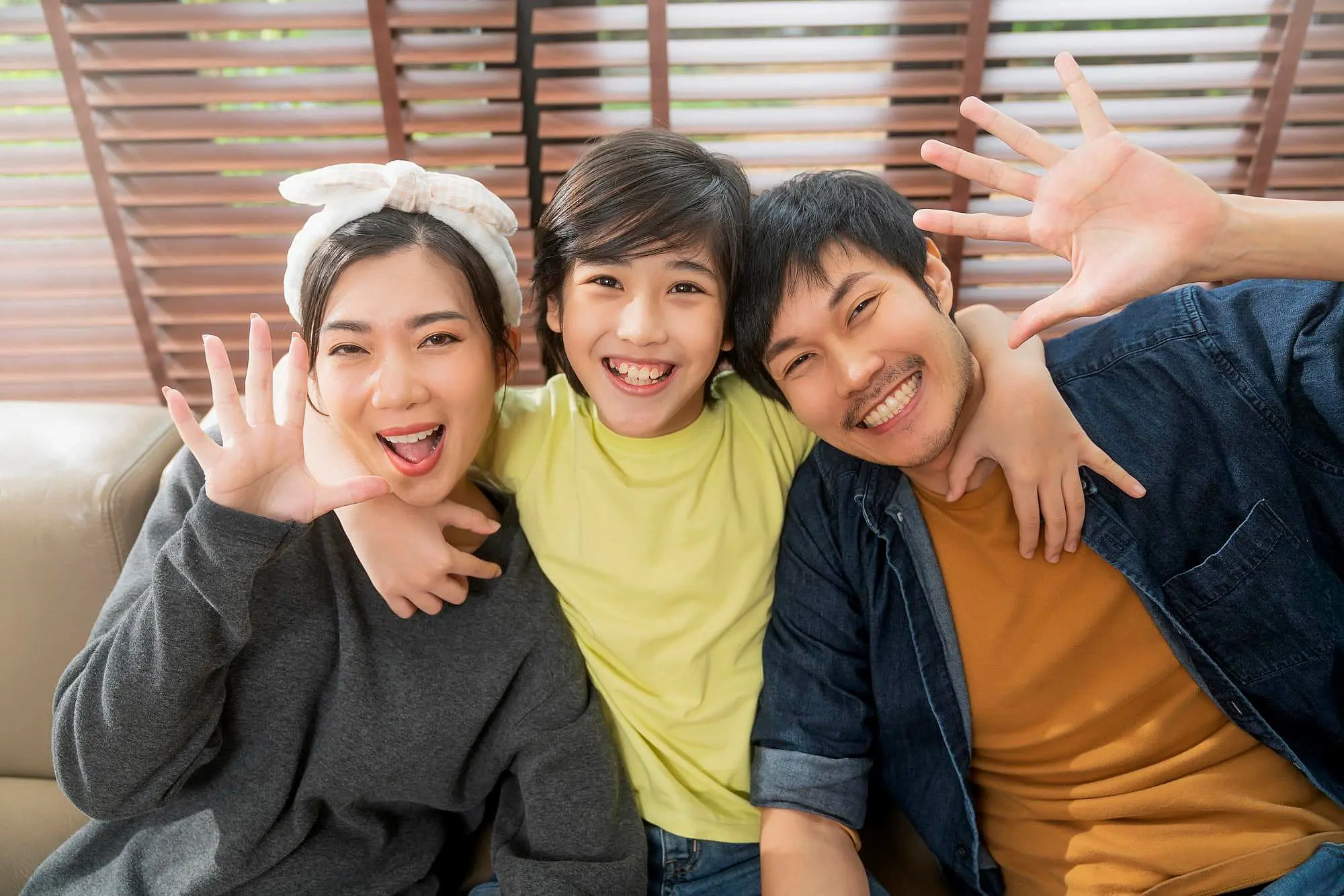 At Happy Smiles Orthodontics in St. Augustine FL, two adults and a child sit on a couch, smiling and waving to celebrate the child’s new Palatal Expander.