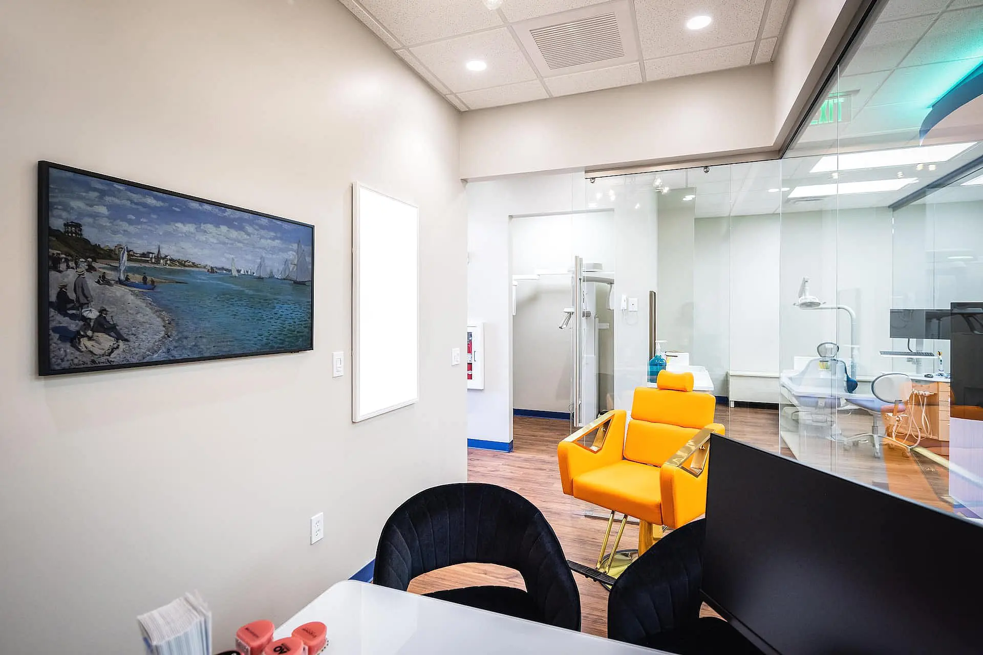At Happy Smiles Orthodontics in St. Augustine, FL, families will find a modern dental office featuring glass walls, orange dental chairs, a desk with a monitor, and a framed seaside painting—an ideal setting for children’s orthodontic care.