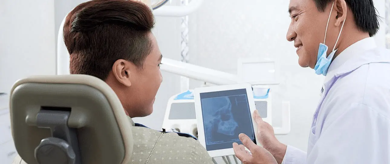 During a consultation at Happy Smiles Orthodontics in St. Augustine, FL, a dentist reviews a dental X-ray on a tablet with a patient and discusses potential jaw surgery options.