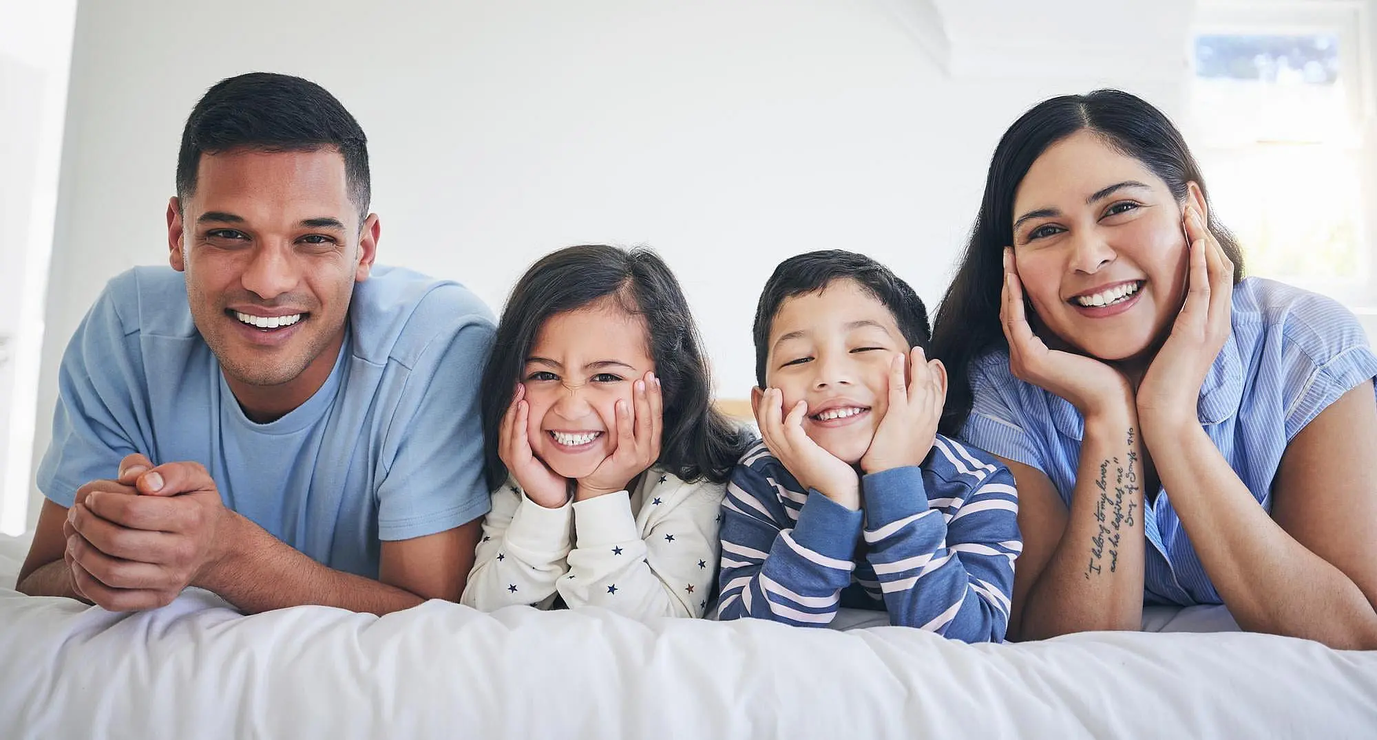 A family of four—two adults and two children—relax on a bed, smiling brightly for the camera after getting affordable braces at Happy Smiles Orthodontics in St. Augustine, FL.