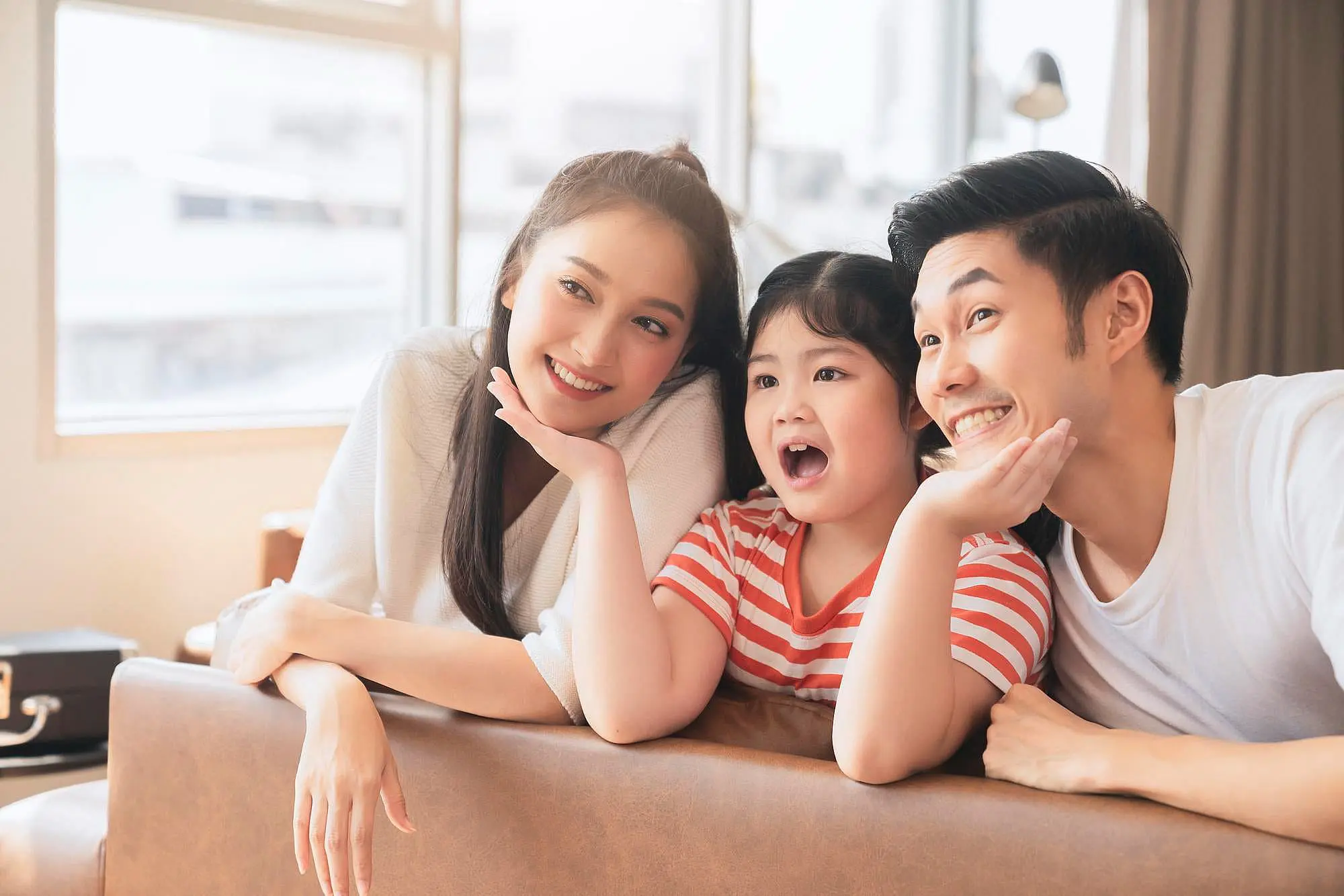 At Happy Smiles Orthodontics in St. Augustine, FL, two adults and a child sit together on a sofa in a bright living room, smiling after receiving affordable Invisalign treatments.