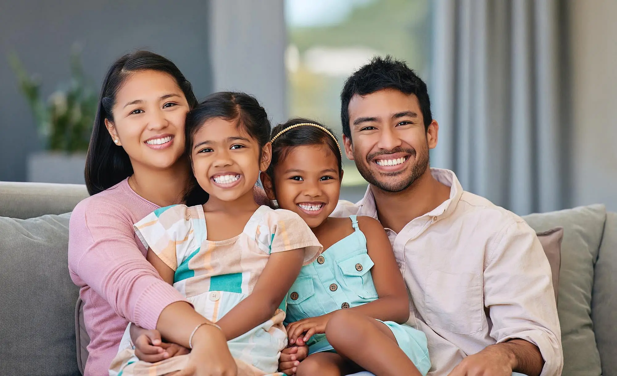A family of four—two adults and two young girls—sits together on a couch, confidently smiling for the camera. Their happy expressions reflect the benefits of orthodontic insurance plans available at Happy Smiles Orthodontics in St. Augustine, FL.