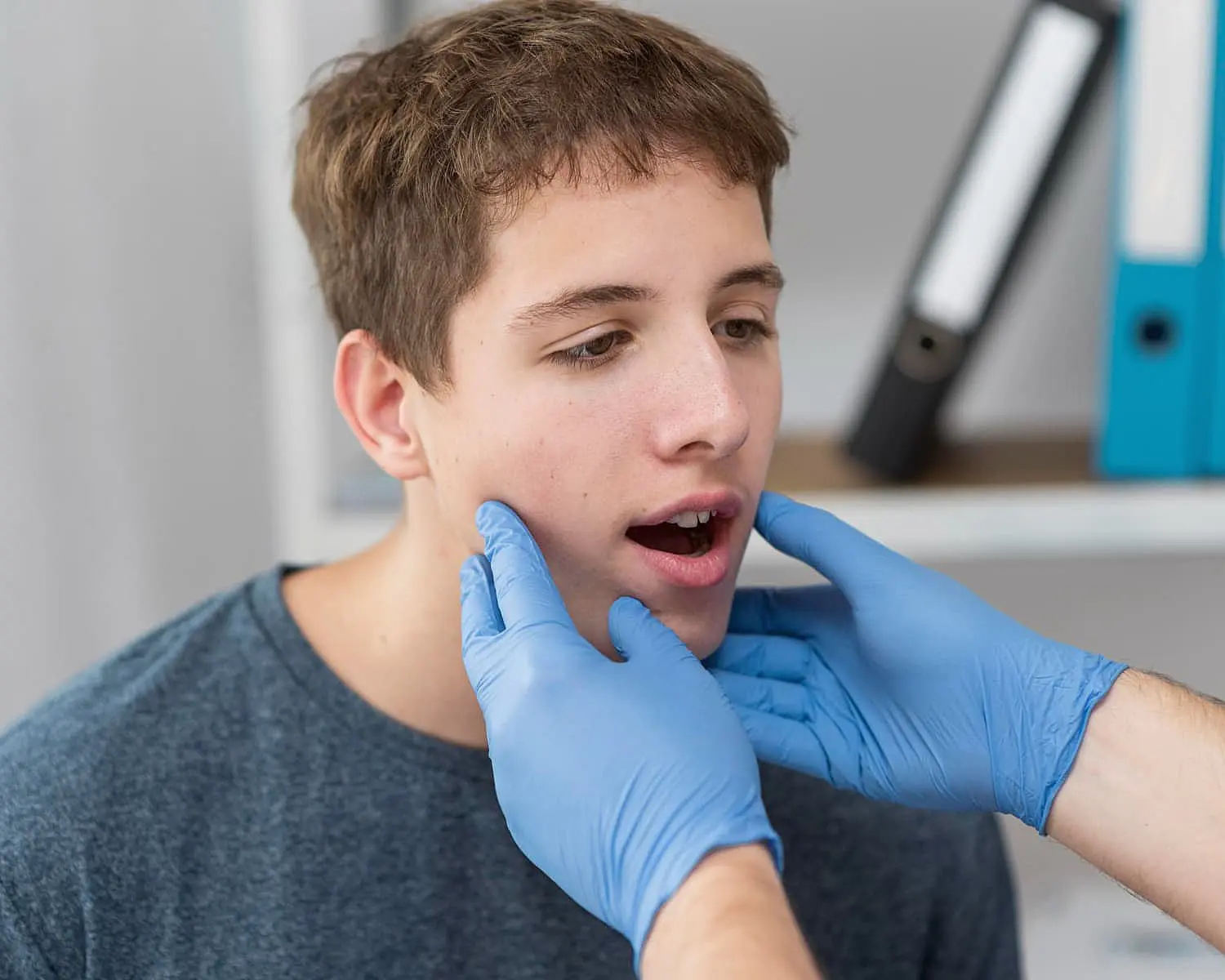 At Happy Smiles Orthodontics in St. Augustine, FL, a healthcare professional in blue gloves examines a teenage boy’s jaw, possibly assessing him for jaw surgery.