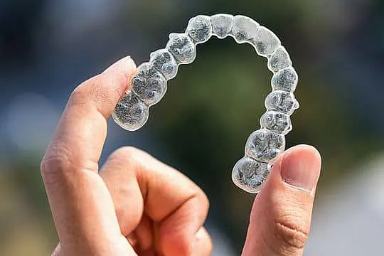 At Happy Smiles Orthodontics in St. Augustine, FL, a hand displays a clear Invisalign aligner for teeth straightening against a blurred background.