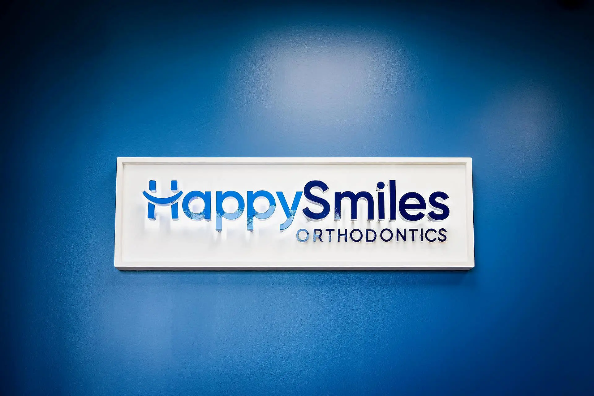 A blue wall displays a white sign for Happy Smiles Orthodontics in St. Augustine, FL.