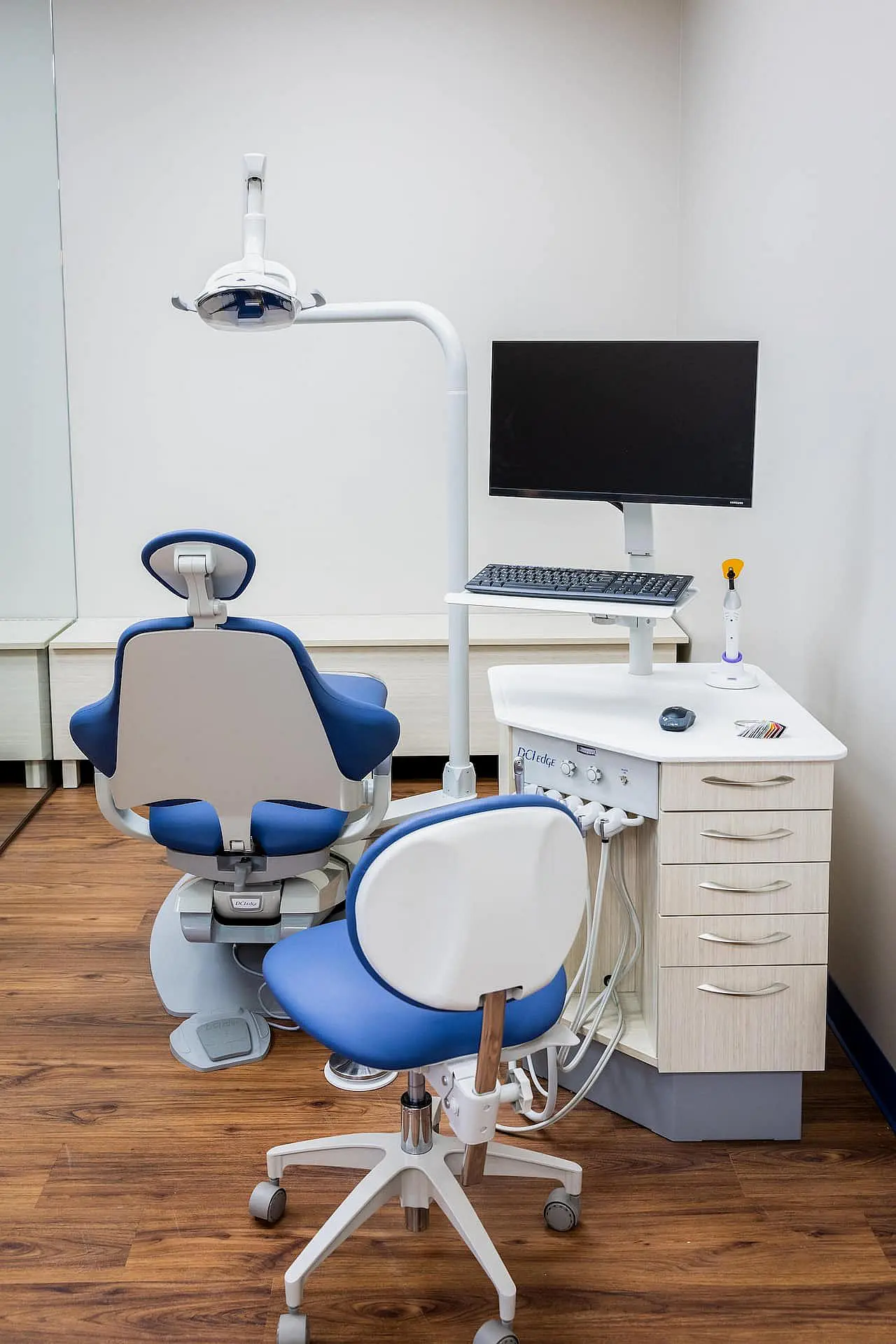 At Happy Smiles Orthodontics in St. Augustine, FL, the modern dental exam room features a blue and white dental chair, dentist’s stool, advanced equipment, and a computer on a cart atop wooden flooring.