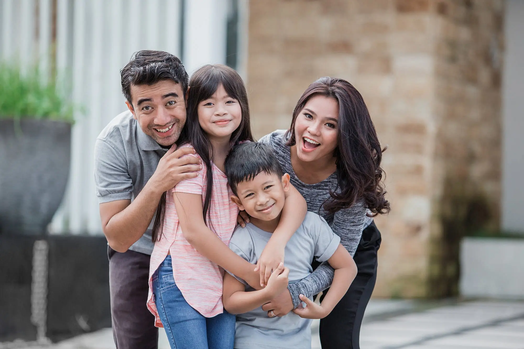 A family of four poses outdoors in casual clothing, with one child proudly displaying a Herbst Appliance—a testament to the quality care at Happy Smiles Orthodontics in St. Augustine, FL.
