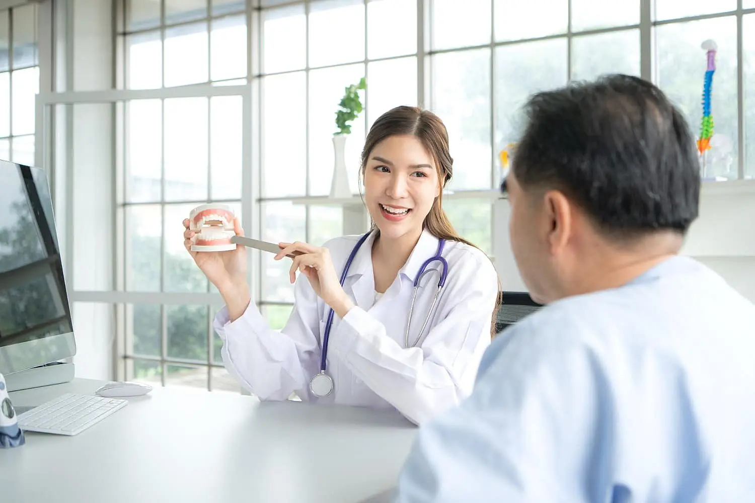 At Happy Smiles Orthodontics in St. Augustine, FL, a female doctor uses a dental model and tool to explain dental care and affordable Invisalign options to a patient in a bright office.
