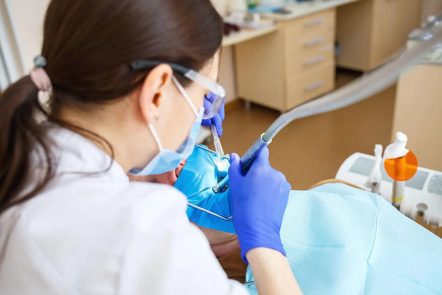 At Happy Smiles Orthodontics in St. Augustine, FL, a dentist in gloves and a mask uses dental tools and a suction device to treat a patient with braces.