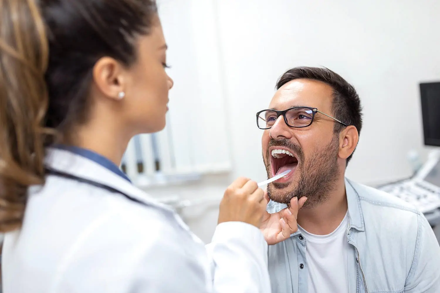During a medical checkup at Happy Smiles Orthodontics in St. Augustine, FL, a healthcare professional uses a tongue depressor to examine a patient’s mouth for issues like tongue thrust.