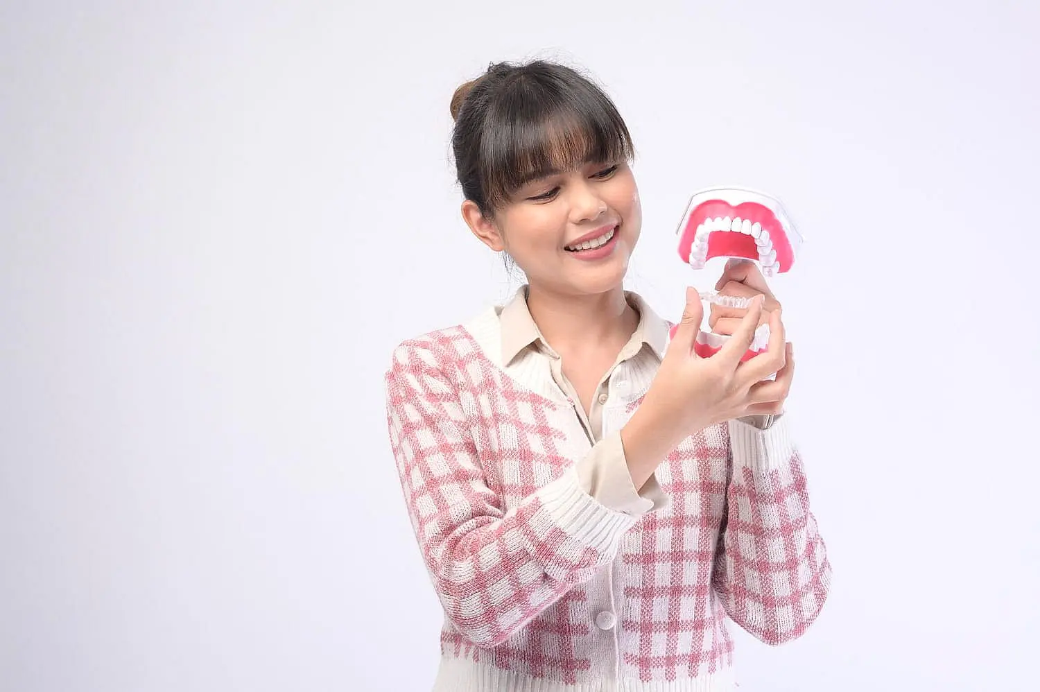 At Happy Smiles Orthodontics in St. Augustine, FL, a woman in a pink checkered sweater examines a dental model with visible teeth, possibly exploring Invisalign treatment.