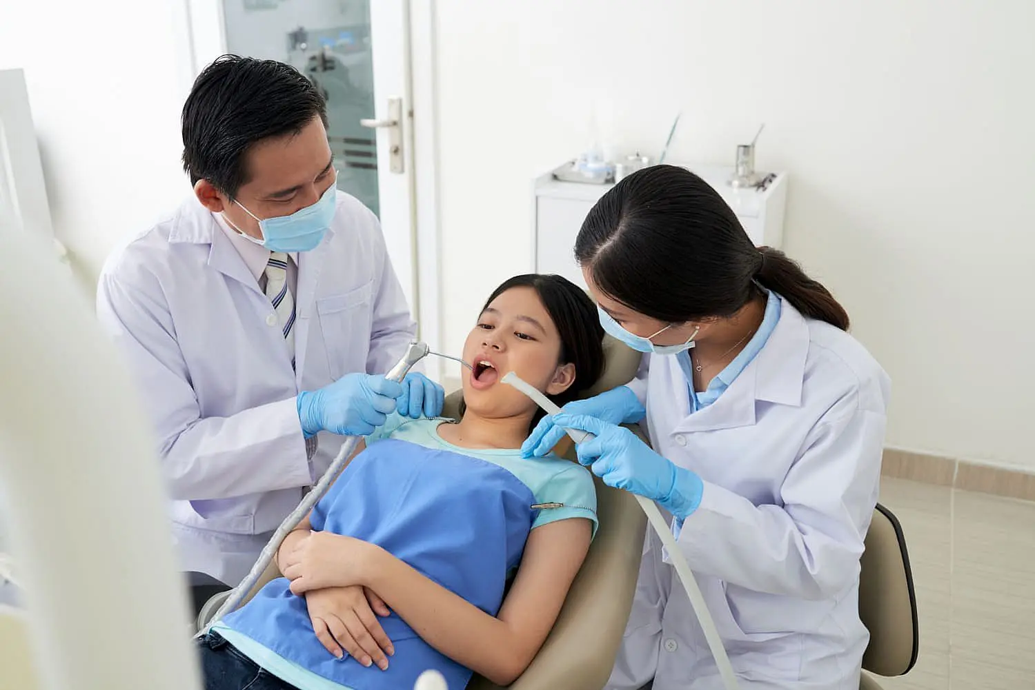 At Happy Smiles Orthodontics in St. Augustine, FL, a dentist and dental assistant examine a young girl’s teeth as she reclines in the chair wearing a protective bib, assessing her need for orthodontic appliances.