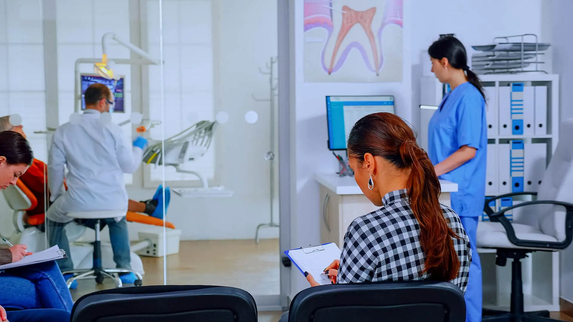 At Happy Smiles Orthodontics in St. Augustine, FL, a woman completes a form in the waiting area as a dental professional reviews orthodontic insurance plans on a computer and a dentist treats a patient nearby.