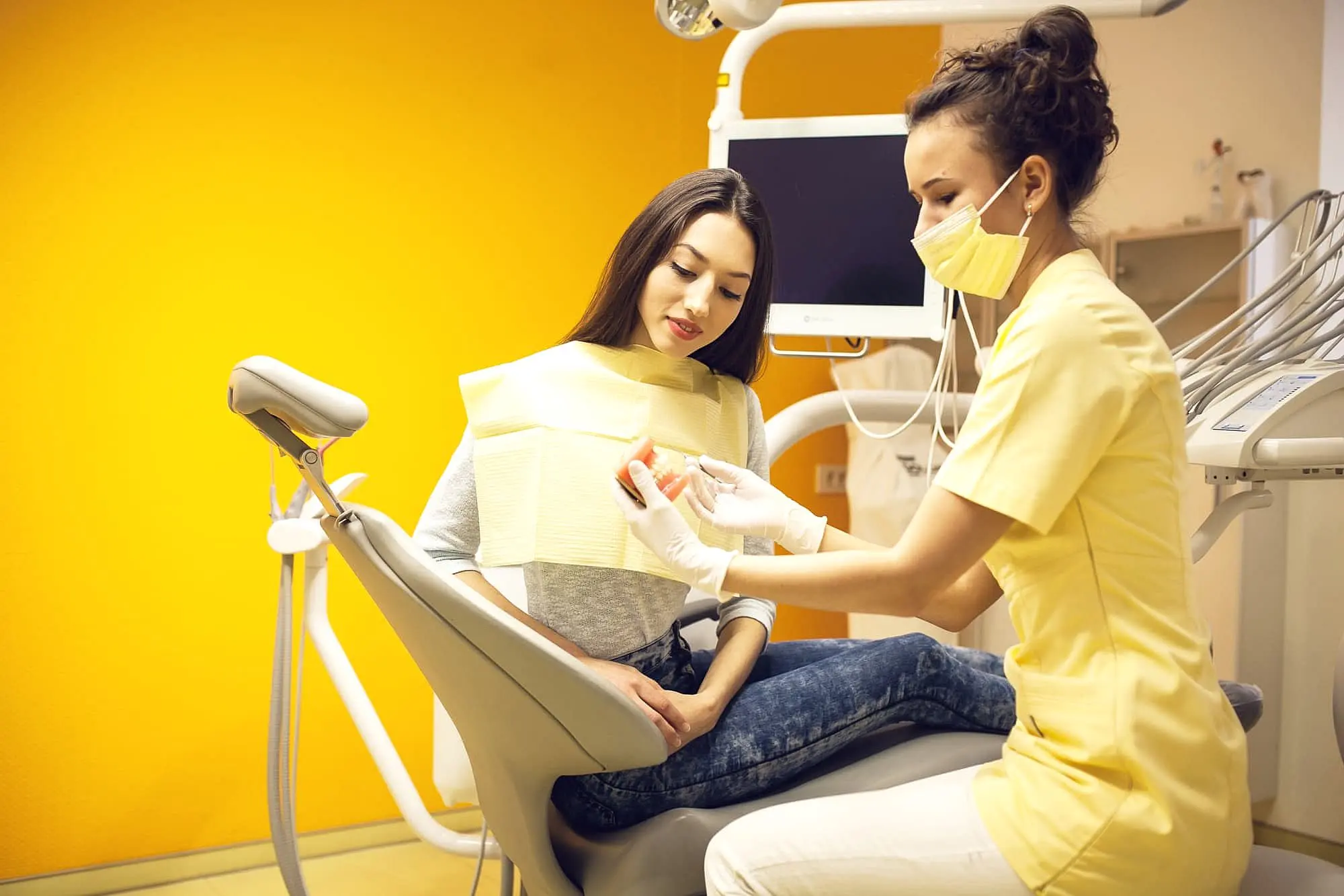 At Happy Smiles Orthodontics in St. Augustine, FL, a dental professional in yellow scrubs reviews orthodontic insurance plans with a patient in the clinic's bright yellow treatment room.