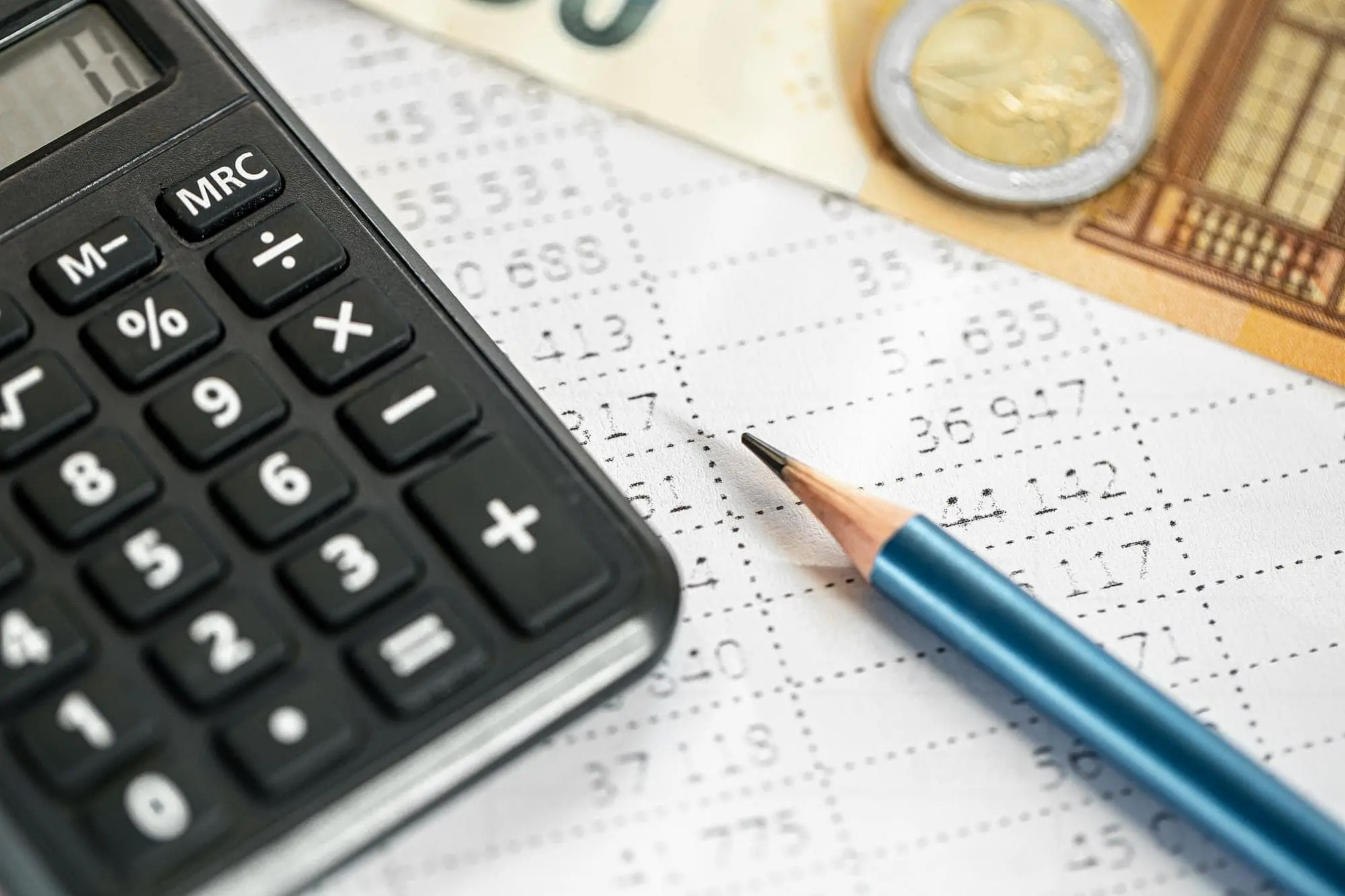 Ideal for visualizing your Braces Payment Plan calculations at Happy Smiles Orthodontics in St. Augustine, FL—a close-up of a black calculator, blue pencil, euro banknote, and coin on a financial spreadsheet.