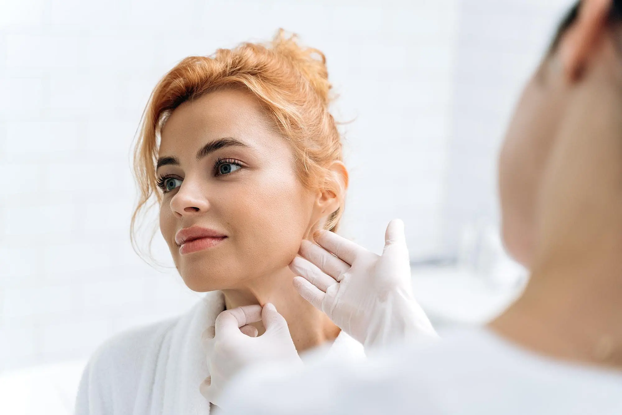 At Happy Smiles Orthodontics in St. Augustine, FL, a healthcare professional wearing gloves examines a woman's neck in a clinical setting to assess her suitability for jaw surgery.