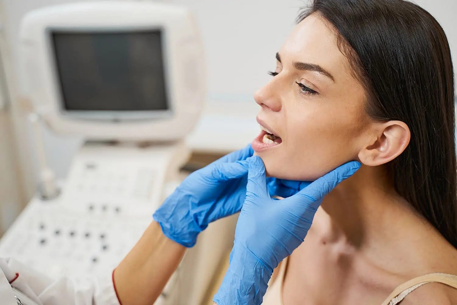 At Happy Smiles Orthodontics in St. Augustine, FL, a healthcare professional wearing blue gloves examines a woman’s jaw and throat—likely to assess her for jaw surgery—as she sits with her mouth open in the medical office.