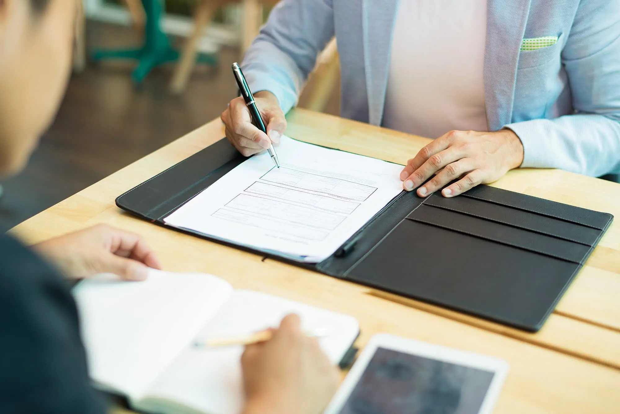 At Happy Smiles Orthodontics in St. Augustine, FL, two people sit at a table—one filling out a document on orthodontic insurance plans in a folder, while the other takes notes in a notebook with a tablet nearby.