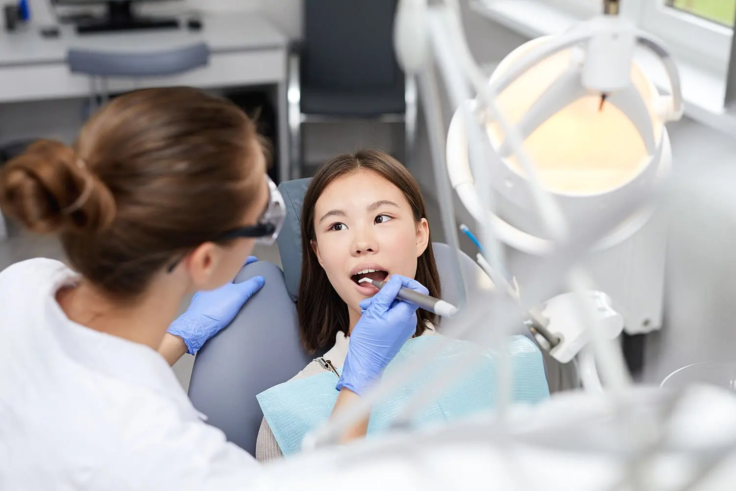At Happy Smiles Orthodontics in St. Augustine, FL, patients receive expert dental care similar to the attentive examinations performed by a children's orthodontist, where dentists use gloves and specialized tools under bright lights to assess oral health.