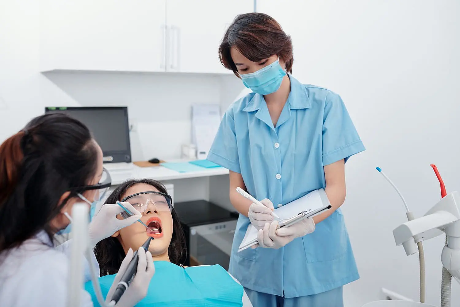 At Happy Smiles Orthodontics in St. Augustine, FL, a dentist treats a patient with metal braces as an assistant in scrubs and a mask takes notes nearby.