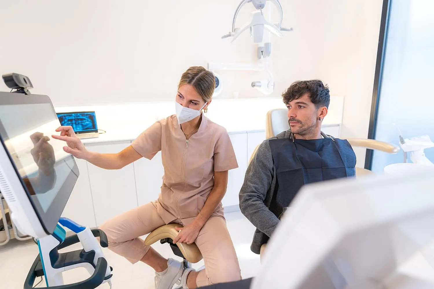At Happy Smiles Orthodontics in St. Augustine, FL, a dental professional in scrubs and a mask presents Invisalign Payment Plan details on a screen to a patient seated in a modern office.