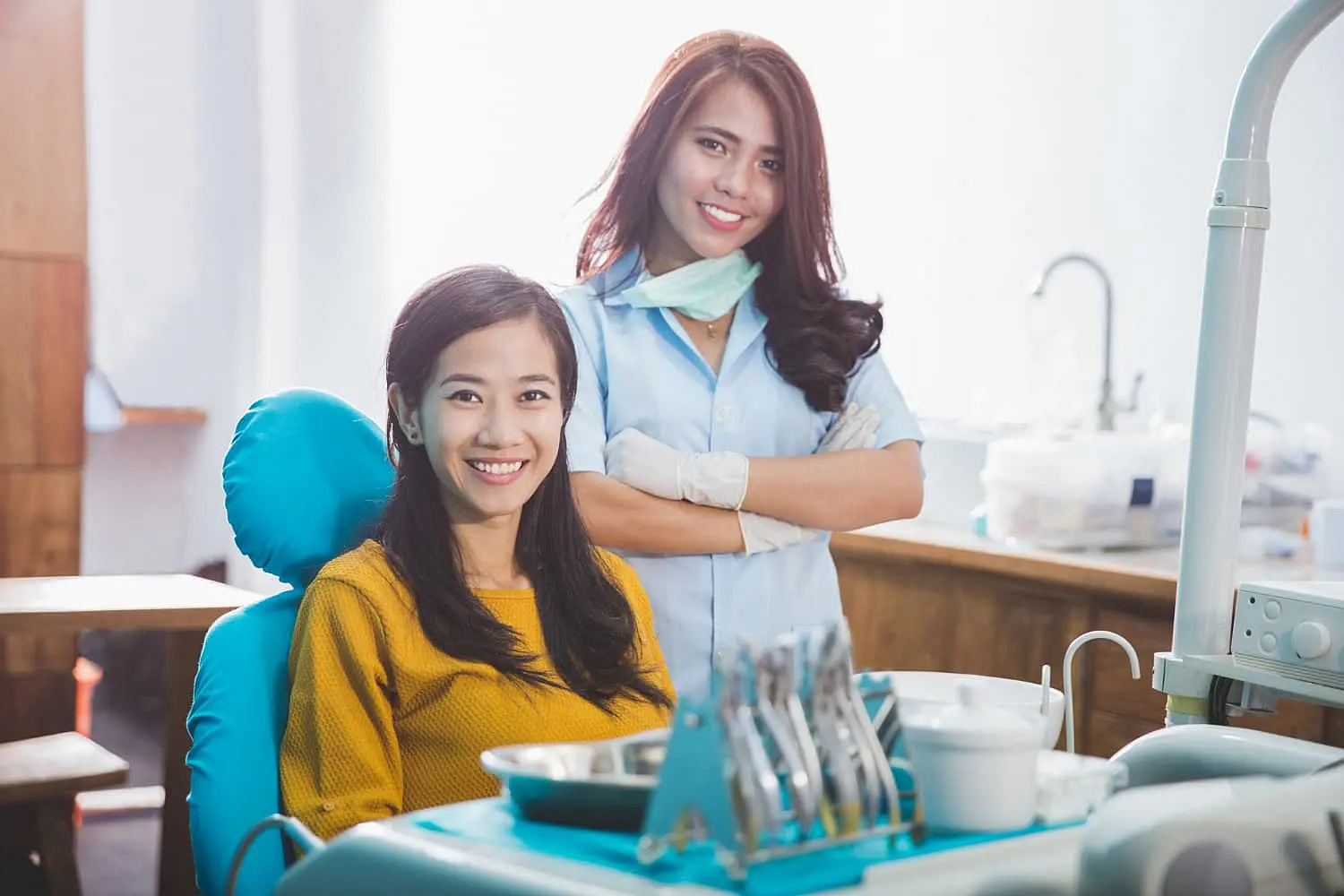 At Happy Smiles Orthodontics in St. Augustine, FL, a woman with metal braces smiles from a dental chair as her dental professional stands beside her, both beaming for the camera in the clinic.