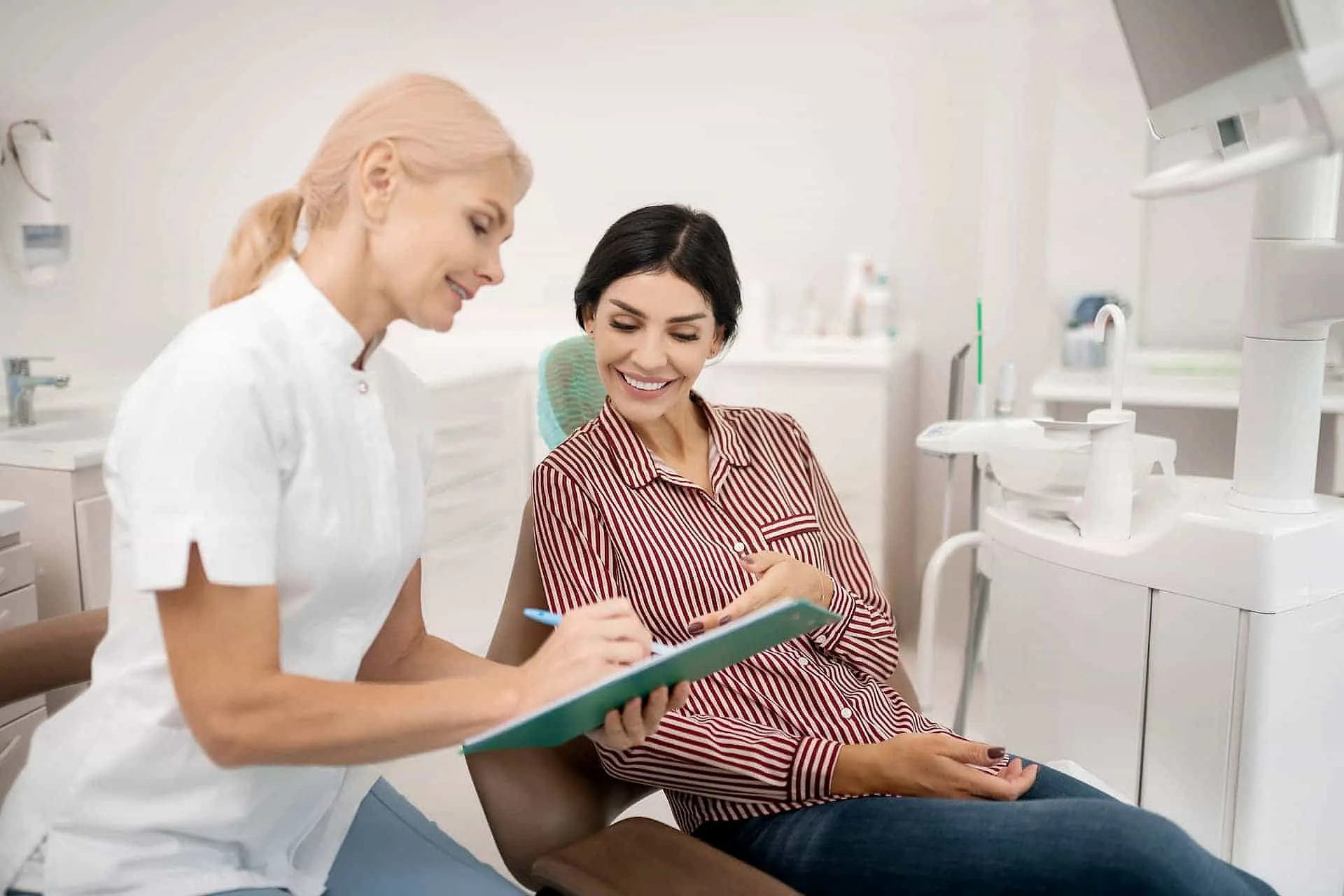 At Happy Smiles Orthodontics in St. Augustine, FL, a dentist explains tongue thrust to a smiling patient while showing a clipboard in their modern office.