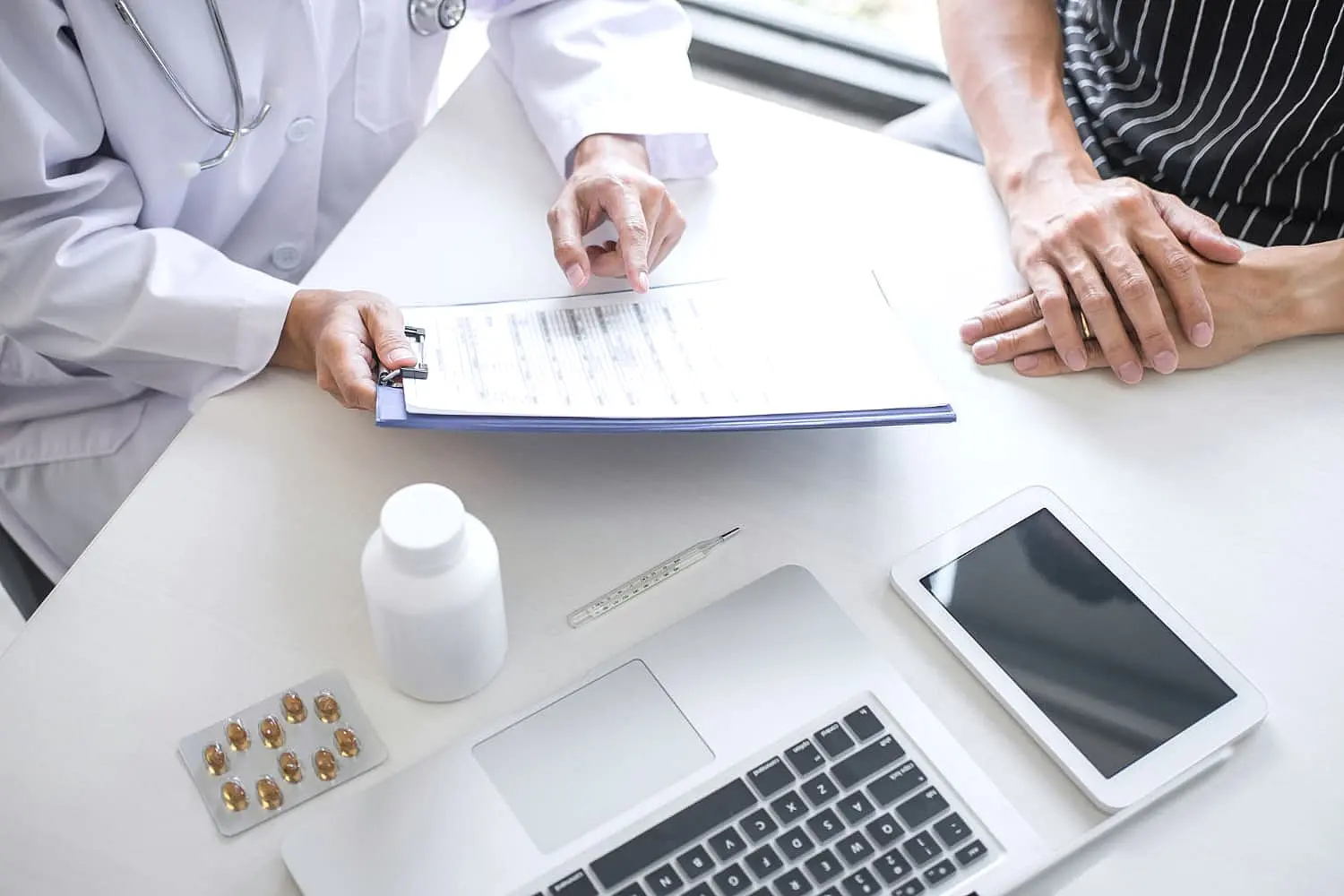 At Happy Smiles Orthodontics in St. Augustine, FL, a doctor discusses orthodontic insurance plans with a patient at a desk, reviewing paperwork alongside a laptop, tablet, and medication on the table.
