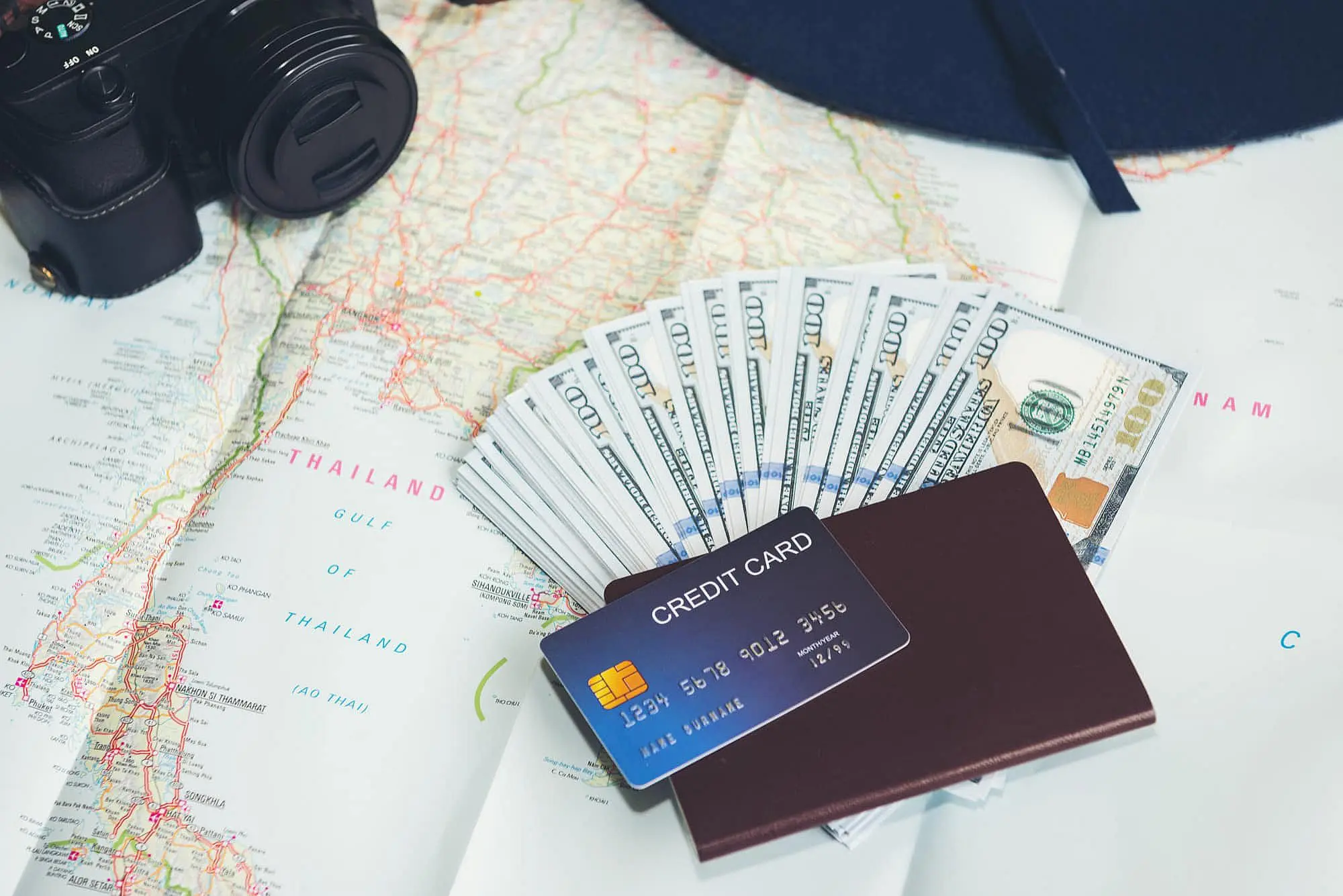Several items, including a camera, a map of Thailand, $100 bills, a passport, and a credit card with an Invisalign Payment Plan from Happy Smiles Orthodontics in St. Augustine, FL, are displayed together to suggest travel preparation.