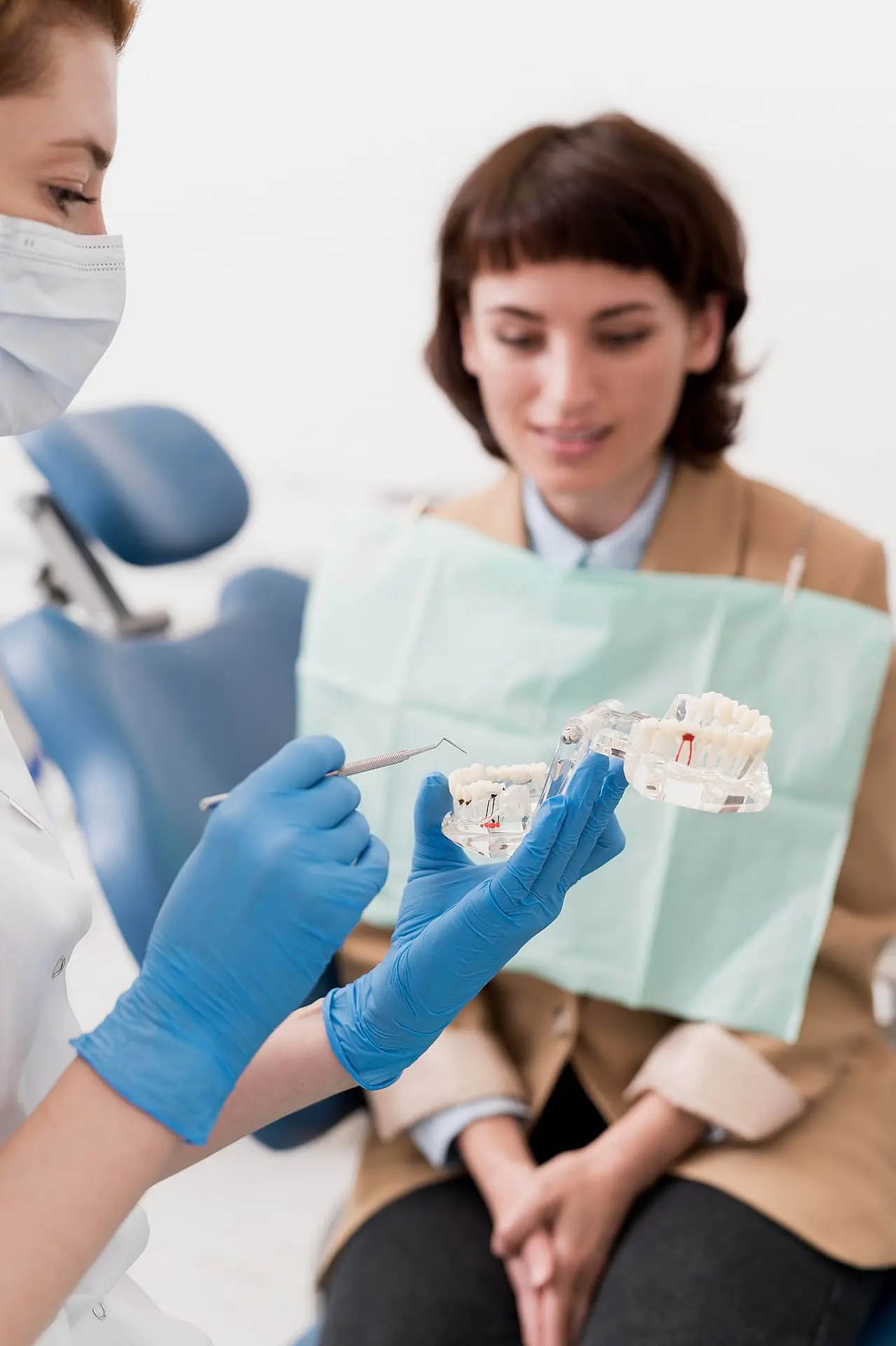 At Happy Smiles Orthodontics in St. Augustine, FL, a dentist in blue gloves uses a teeth model to explain dental health and the benefits of jaw surgery to an attentive patient.