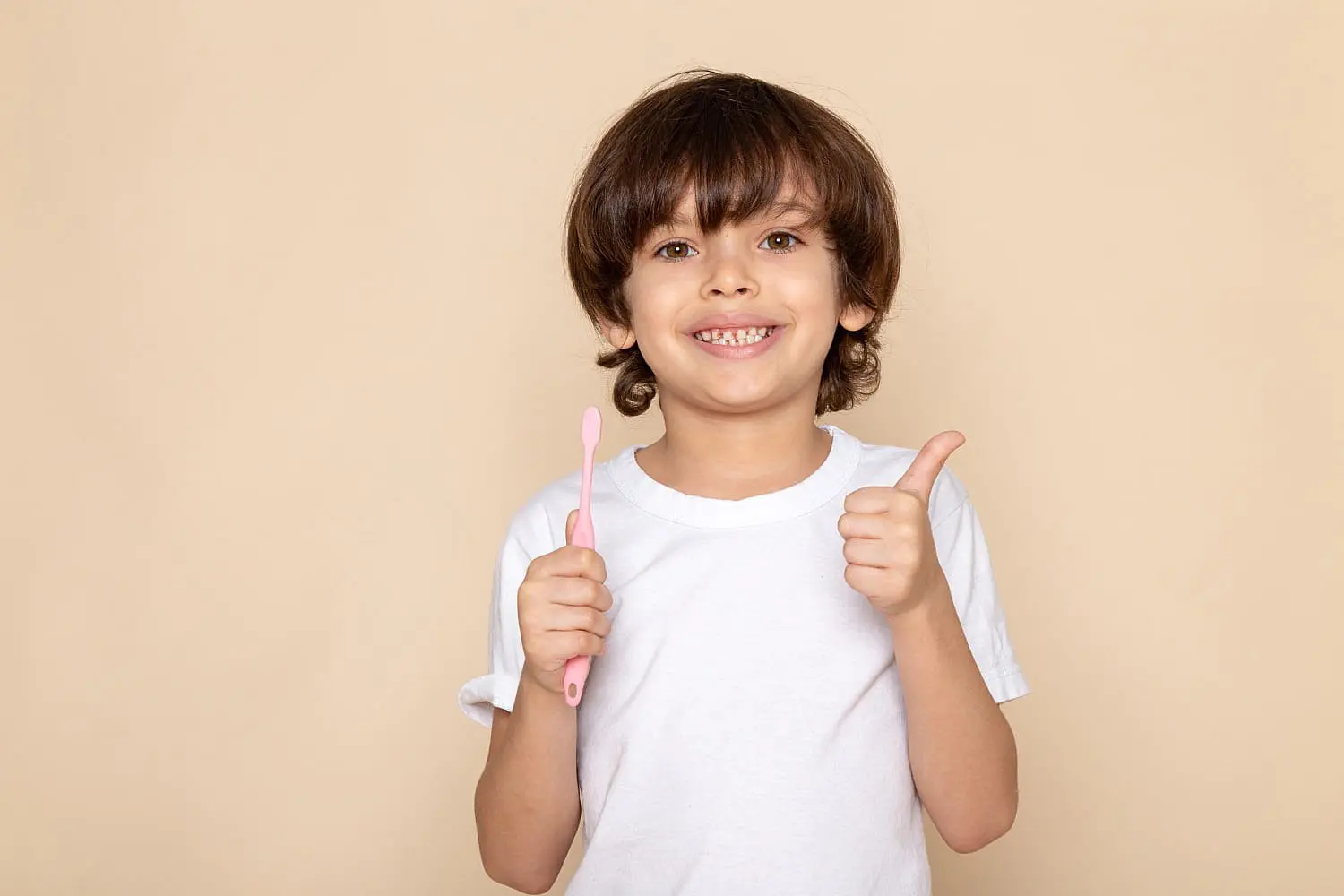 A smiling child with braces gives a thumbs up and holds a pink toothbrush against a beige background, highlighting the confidence gained at Happy Smiles Orthodontics in St. Augustine, FL.