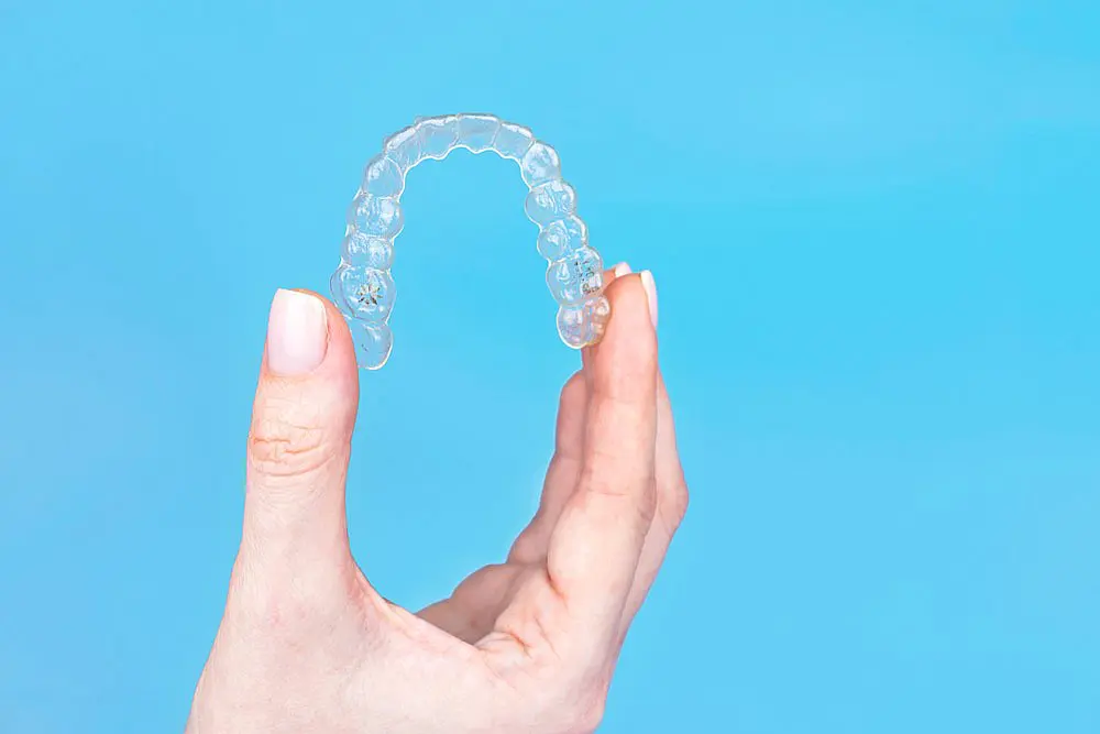 Featuring a hand holding a clear dental aligner against a light blue background, this image showcases the benefits of an Invisalign Payment Plan at Happy Smiles Orthodontics in St. Augustine, FL, for achieving a straighter smile.