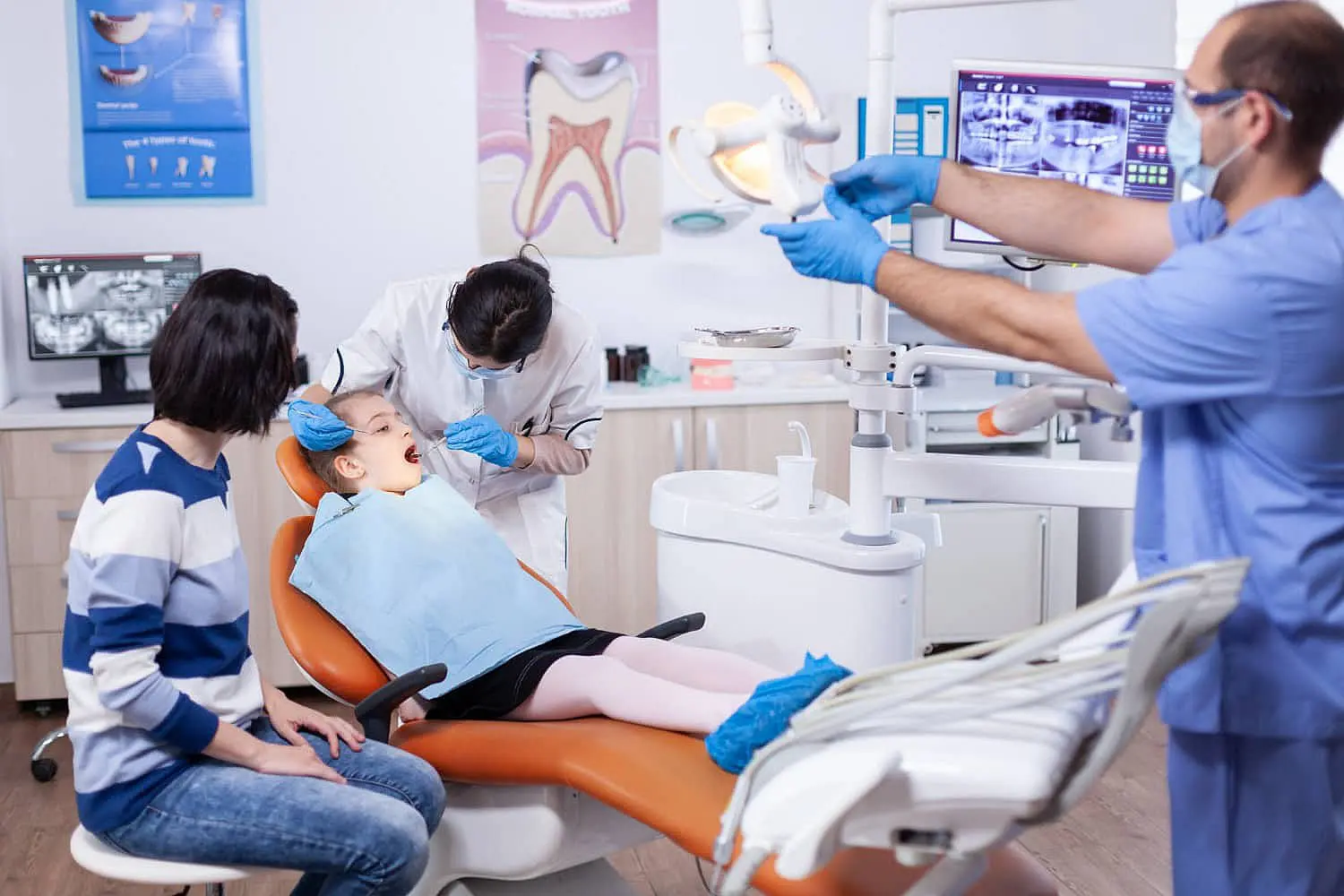 At Happy Smiles Orthodontics in St. Augustine, FL, a child is examined for tongue thrust by a dentist and assistant while an adult sits nearby; dental equipment and monitors are present in the room.