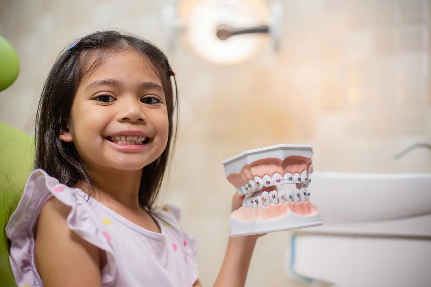 At Happy Smiles Orthodontics in St. Augustine, FL, a young girl beams with excitement for affordable braces as she holds a dental model with braces in the clinic.