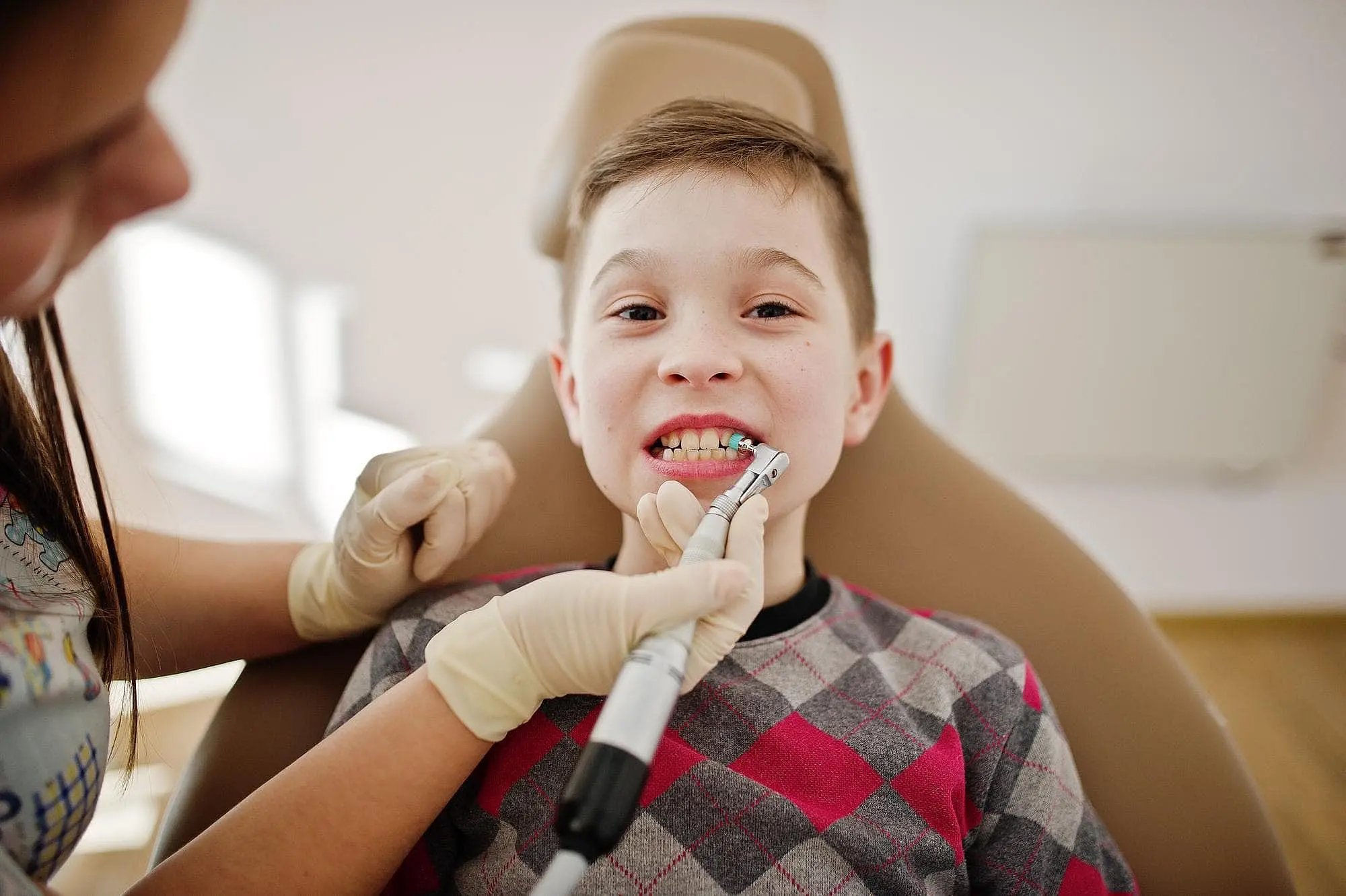 At Happy Smiles Orthodontics in St. Augustine, FL, a children's orthodontist in gloves uses dental tools to clean a child's teeth as they sit in the dental chair.