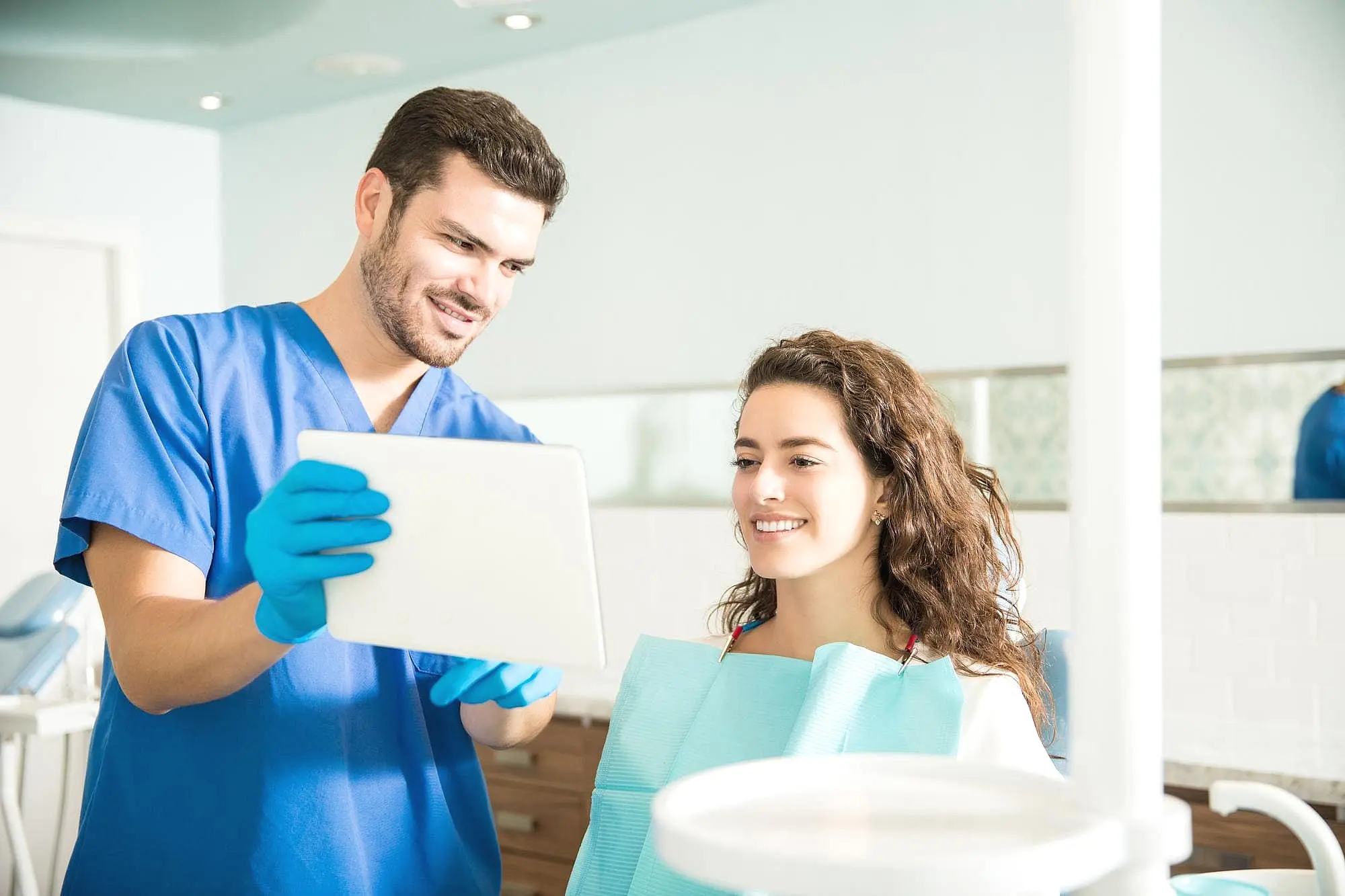 At Happy Smiles Orthodontics in St. Augustine, FL, a dentist in blue scrubs and gloves reviews a digital tablet with a smiling patient during a free orthodontic consultation.