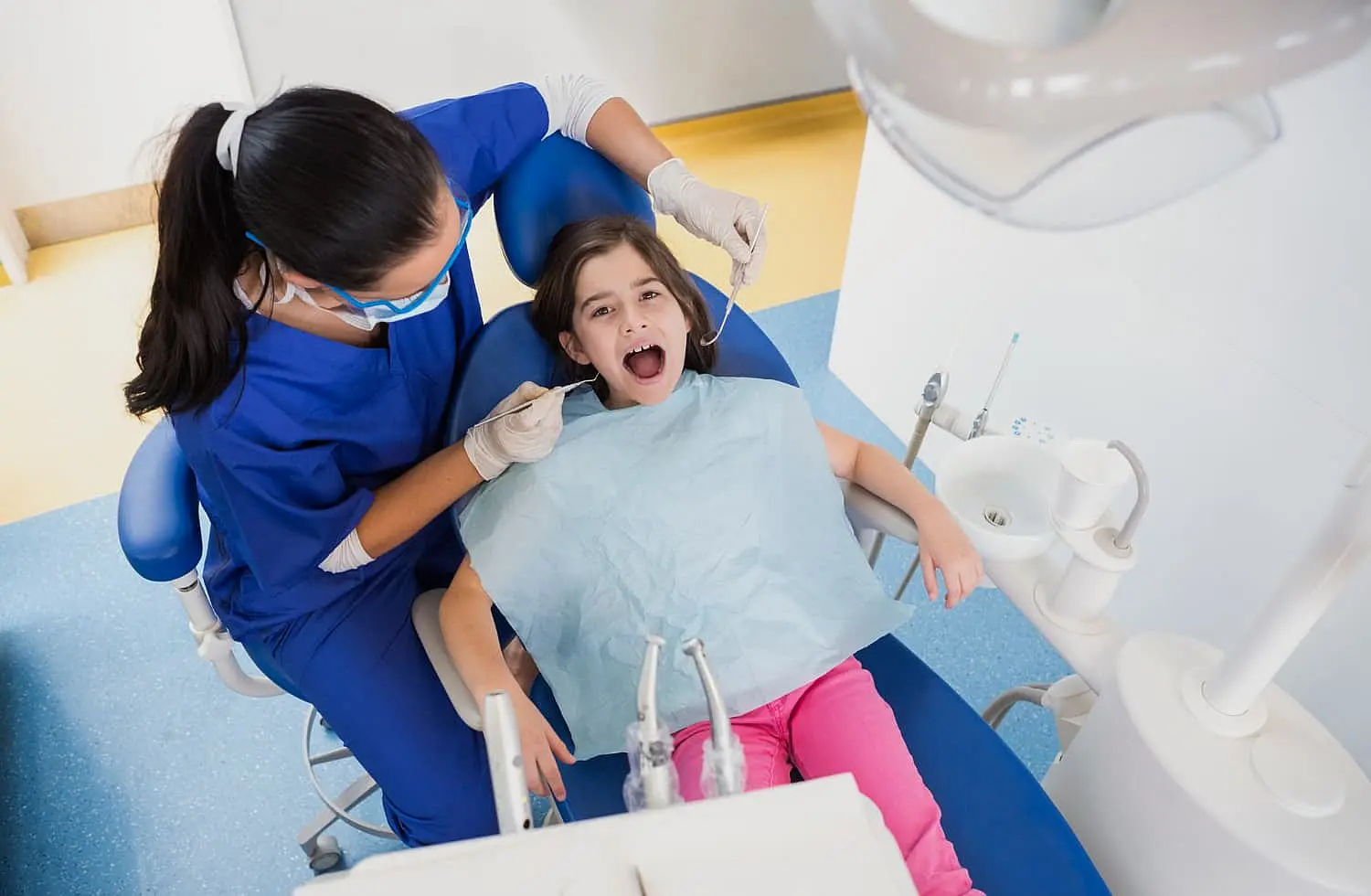 At Happy Smiles Orthodontics in St. Augustine, FL, a dentist in scrubs examines a young girl’s open mouth with dental tools, assessing her need for orthodontic appliances.