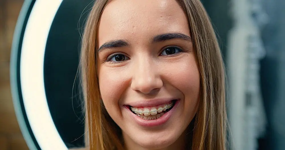 Happy Smiles Orthodontics A young person with long hair and clear braces, smiling brightly in front of a circular light, represents the confidence gained from Happy Smiles Orthodontics in St. Augustine, FL.
