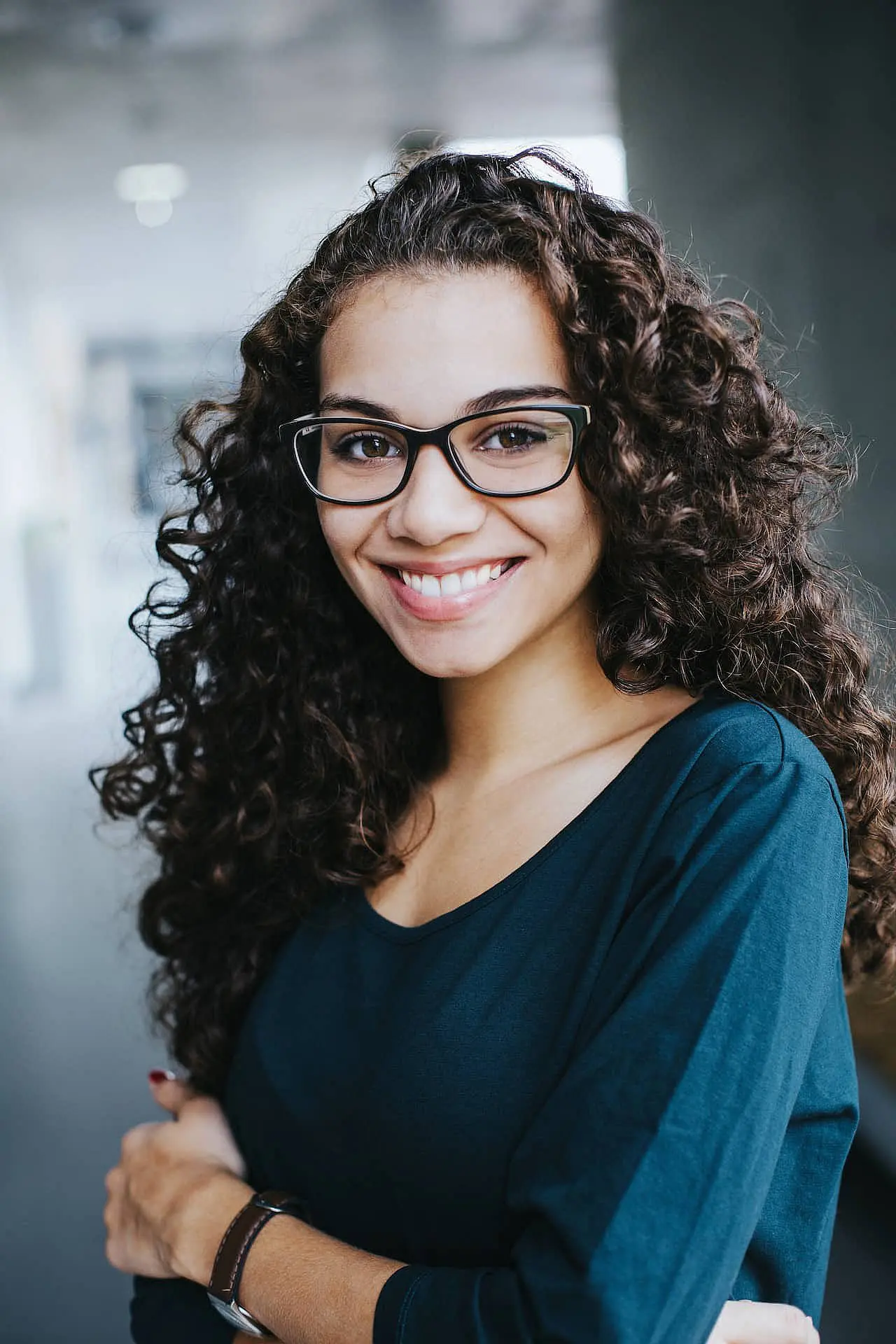 At Happy Smiles Orthodontics in St. Augustine, FL, a woman with long curly hair and glasses, dressed in a dark teal top, smiles warmly at the camera against a softly blurred indoor background, reflecting professional and friendly care.