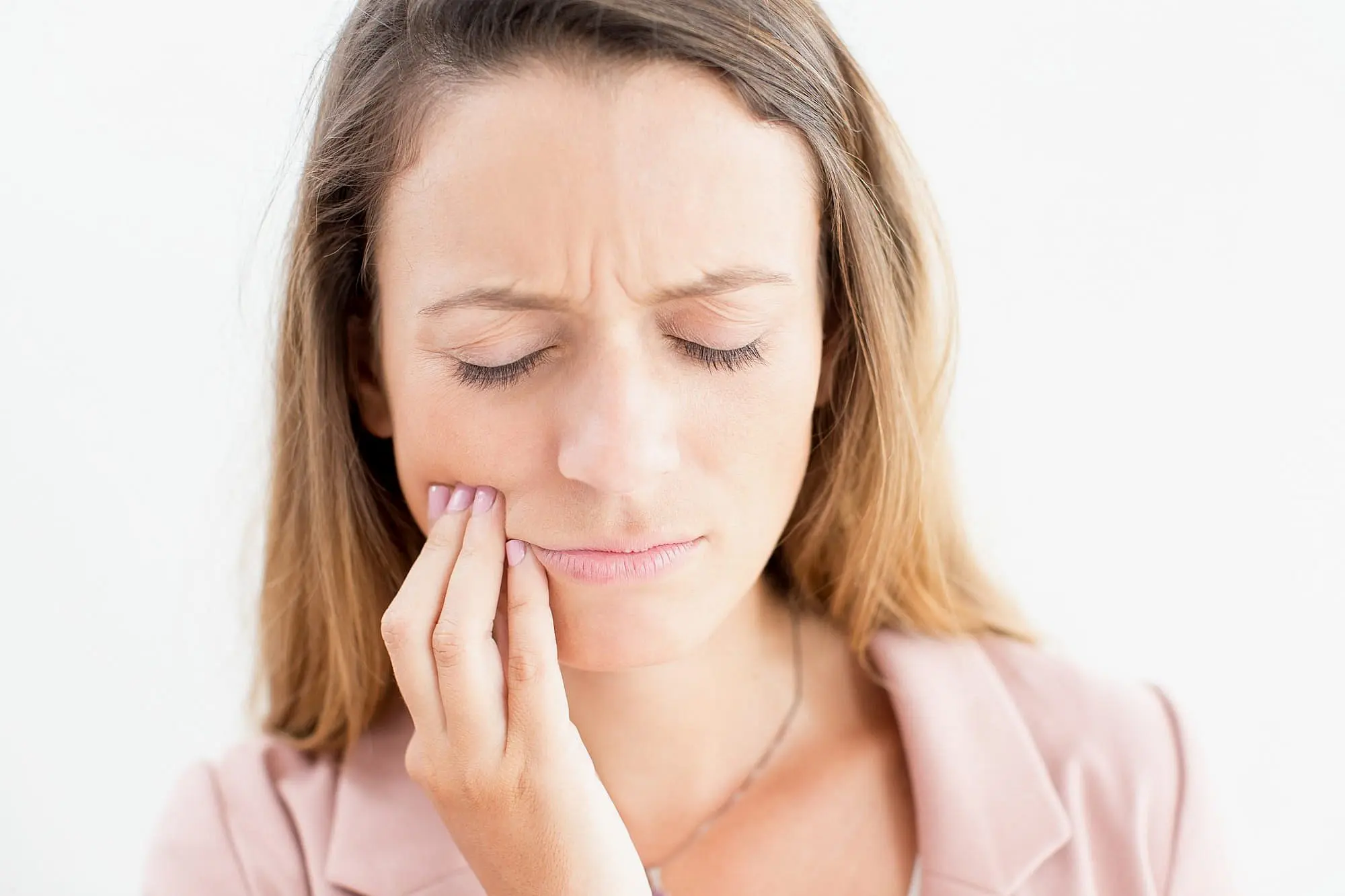 A woman with closed eyes presses her hand to her cheek, looking like she's feeling tooth or jaw pain—possibly weighing the discomfort of Invisalign vs braces at Happy Smiles Orthodontics in St. Augustine, FL.