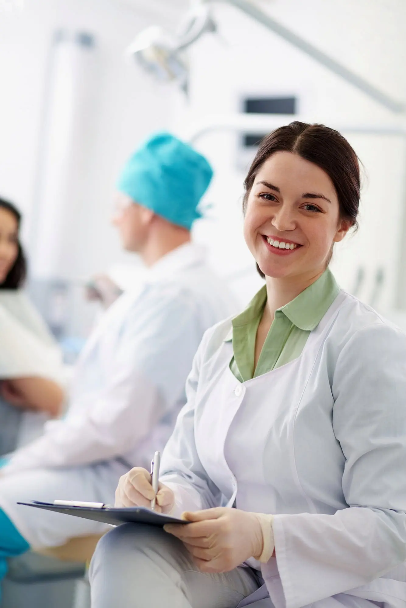 At Happy Smiles Orthodontics in St. Augustine, FL, a female orthodontist in a white coat smiles at the camera with clipboard in hand, while two team members—including one in a surgical cap—are visible in the background.