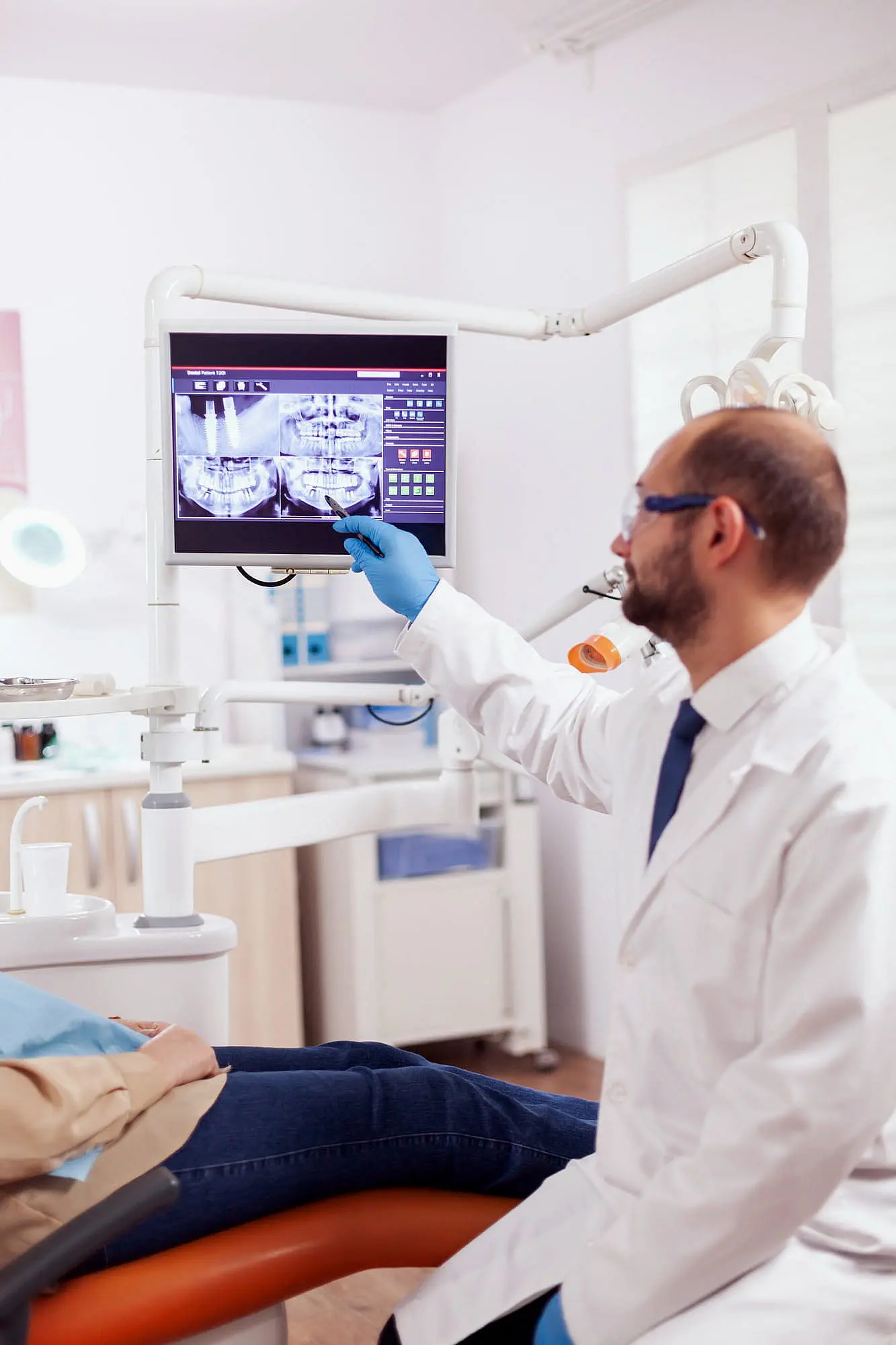 At Happy Smiles Orthodontics in St. Augustine, FL, a dentist in a white coat and gloves reviews a dental X-ray on screen, discussing potential jaw surgery with a patient in the chair.
