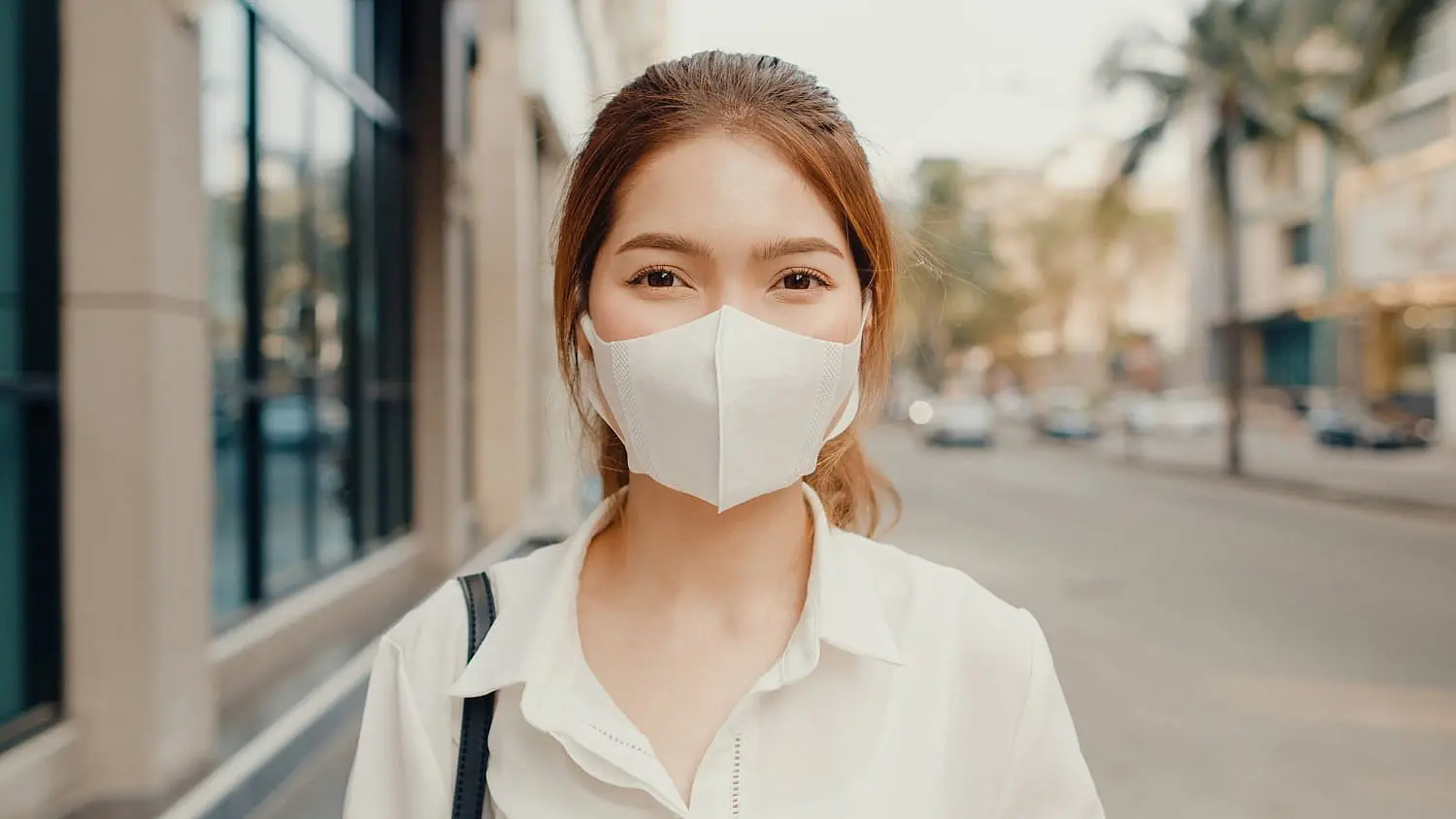 Outdoors on a city street in St. Augustine, FL, a woman in a white face mask and blouse demonstrates how Happy Smiles Orthodontics ensures protection—even for mouth breathers.