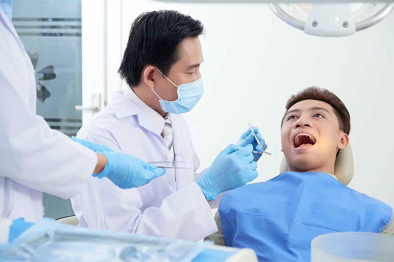 At Happy Smiles Orthodontics in St. Augustine, FL, a dentist wearing a mask examines a patient’s mouth for tongue thrust using dental tools, assisted by a staff member in the clinic.