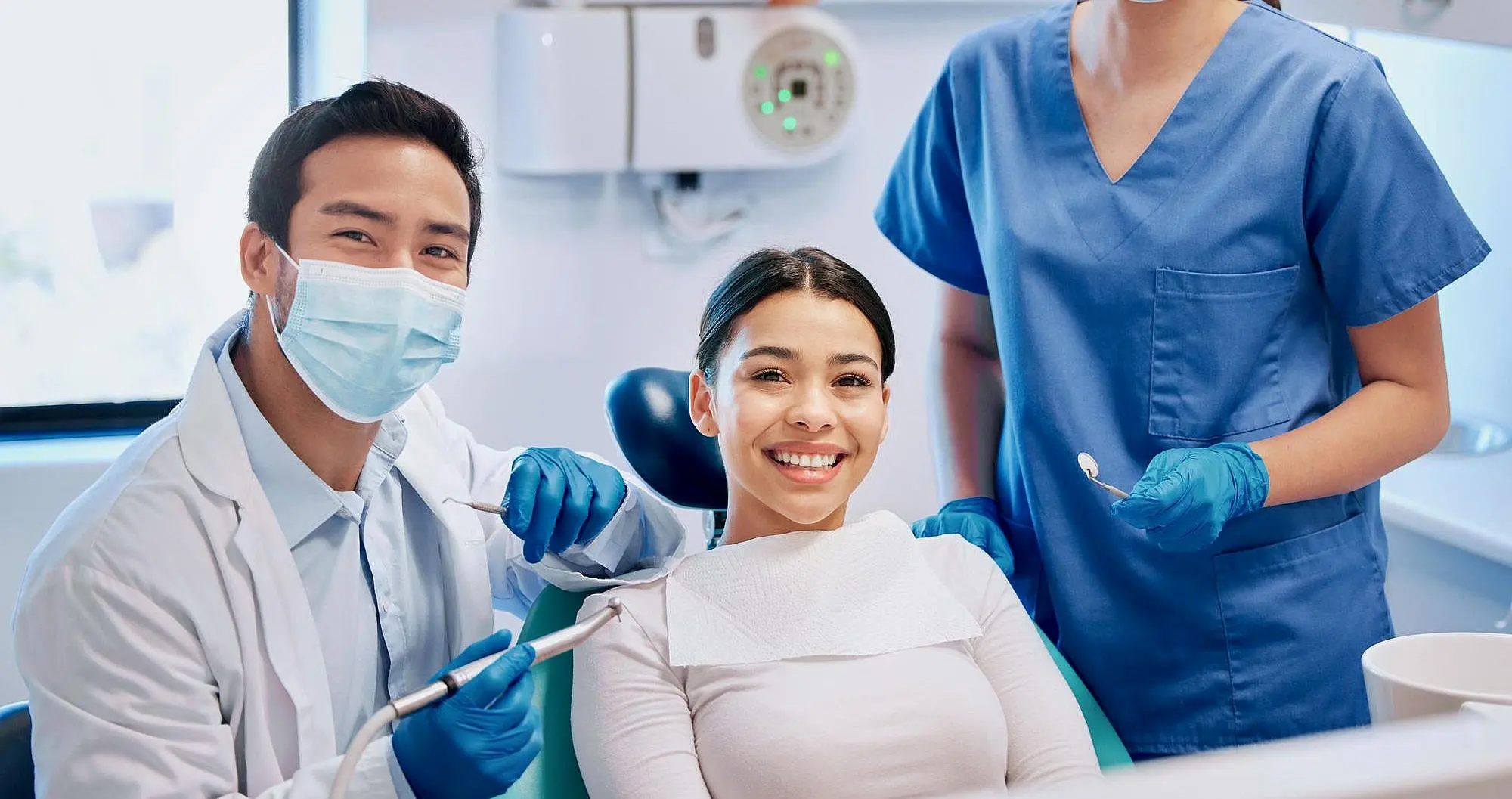 At Happy Smiles Orthodontics in St. Augustine FL, a patient with an underbite give smile from the dental chair as two masked and gloved professionals smile beside her.
